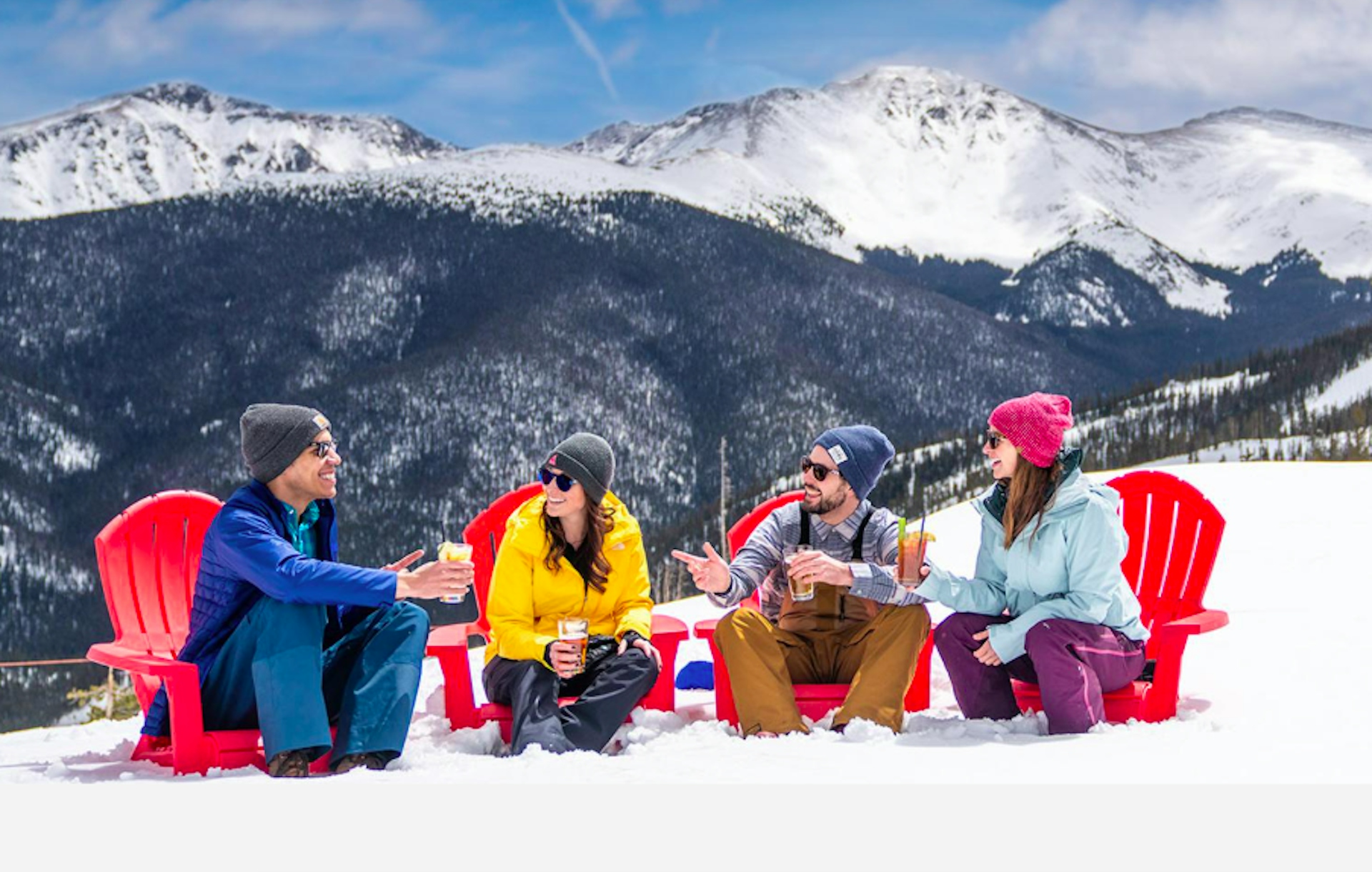 four people sitting outside at an Ikon Pass ski resort talking and laughing holding drinks