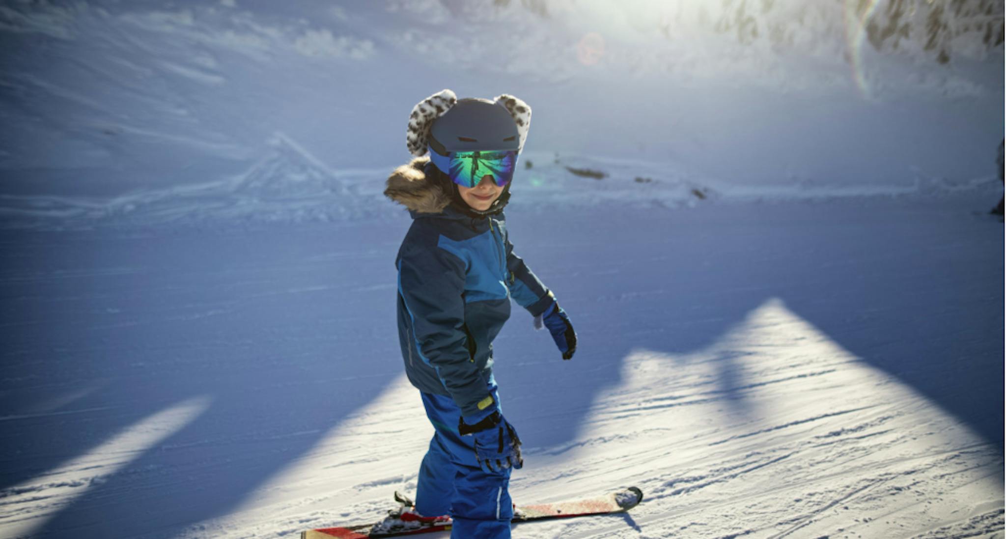 small child smiling on skis on a sunny ski slope