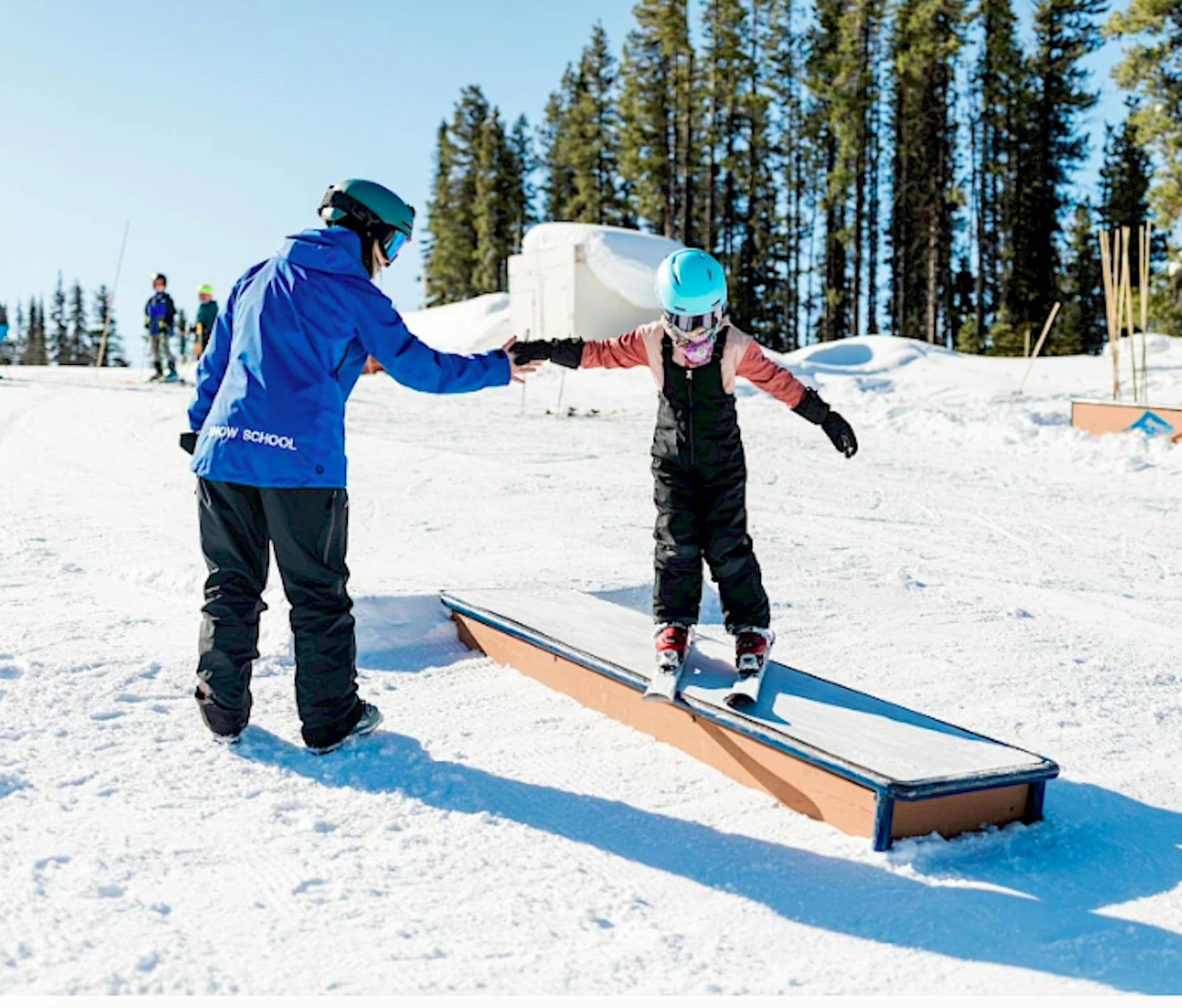 parent holding kid's hand while they ski a box ramp at Revelstoke ski resort