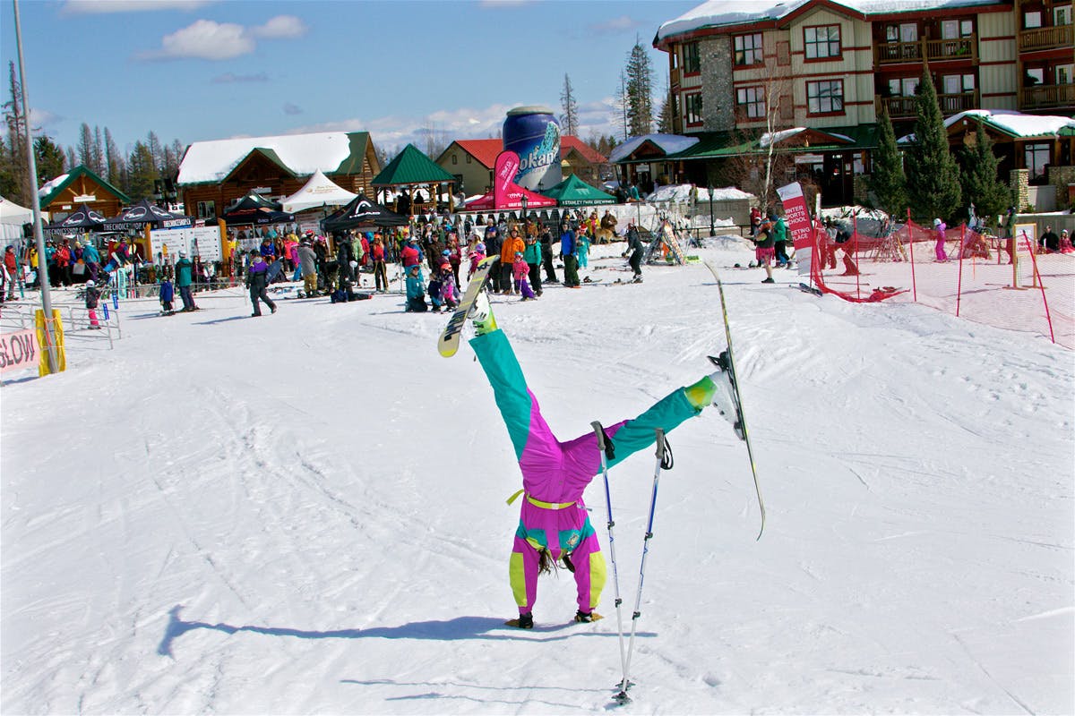 A female skier in 1990s vintage-style ski suit clowning around at basecamp at Kimberley Alpine Resort in Kimberley, British Columbia, Canada.