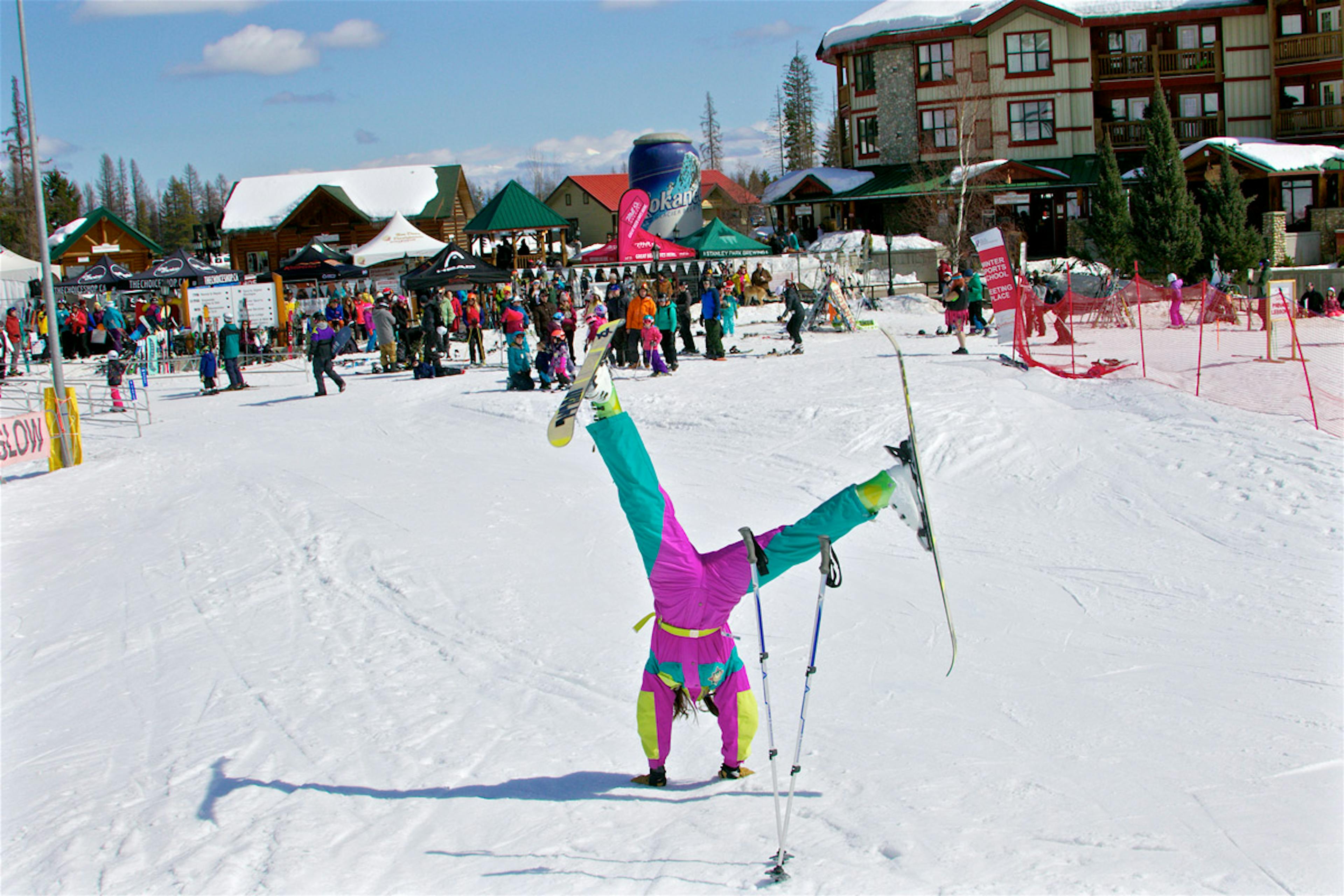 A female skier in 1990s vintage-style ski suit clowning around at basecamp at Kimberley Alpine Resort in Kimberley, British Columbia, Canada.