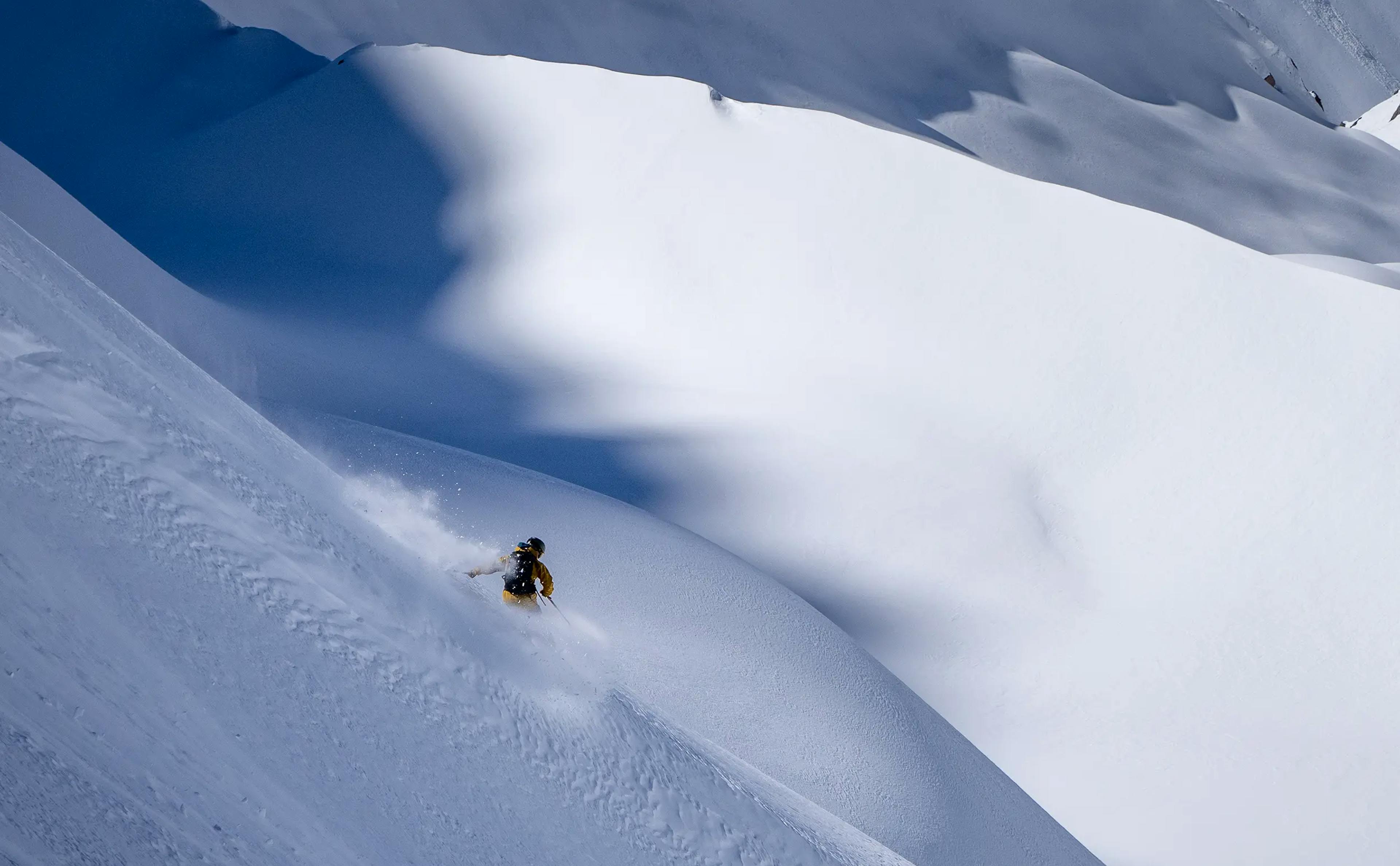 A skier of undiscernible gender in yellow ski jacket hitting the slopes at Valle Nevado in Chile, South America.