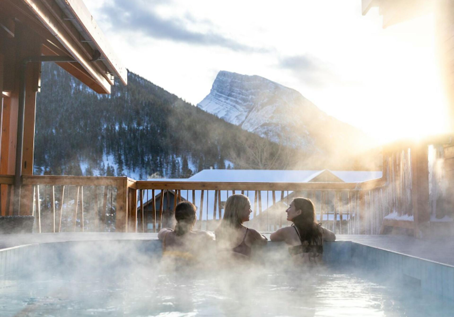 3 friends soak in the steamy hot pools overlooking snowy mountains at Banff Upper Hot Springs