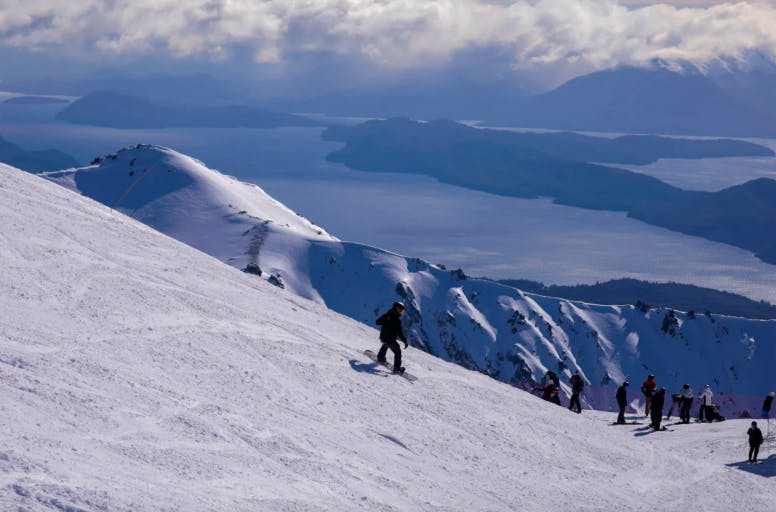 riders on a snowy slope overlooking lakes and mountains at Cerro Catedral ski resort