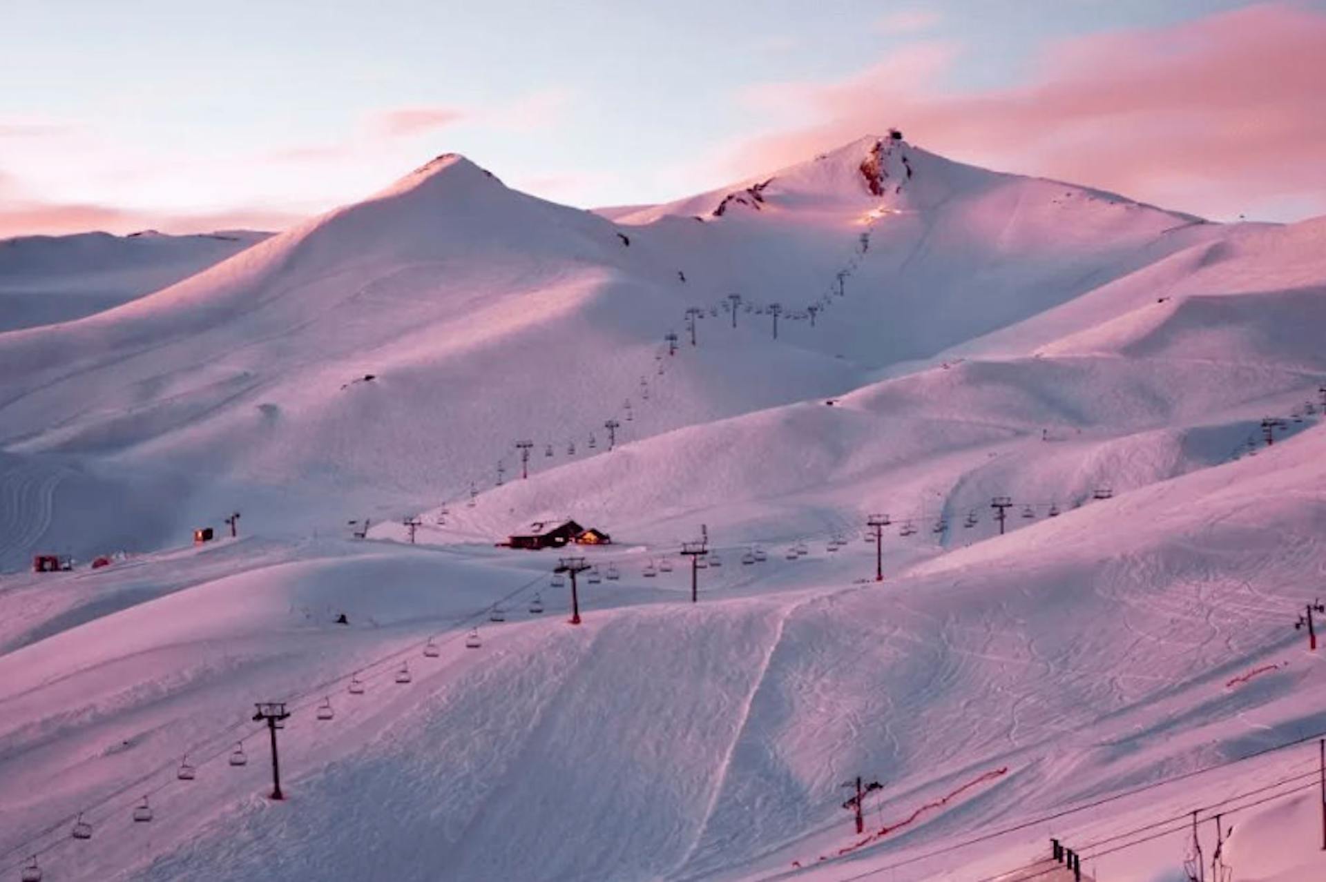 the sun sets on the snowy slopes of Valle Nevado Chile ski resort turning it to a pink hue color