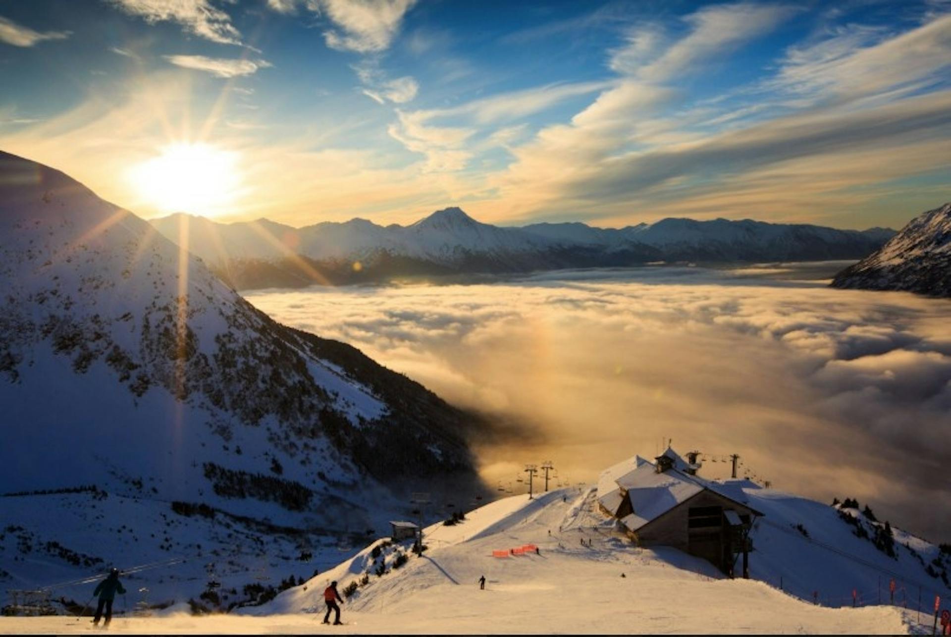 A bird's eye view of a lodge and ski run as the sun sets past the snowy mountains at Alyeska Resort in Alaska