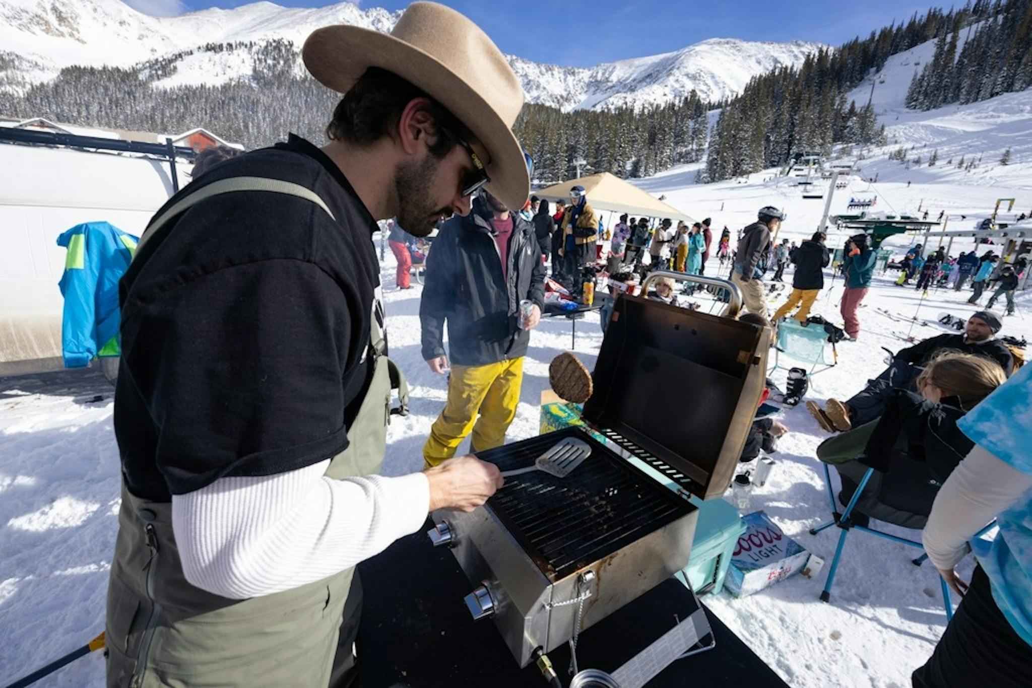 Man wearing cowboy hat flipping hamburger on a barbeque grill at The Beach at Arapahoe Basin Resort