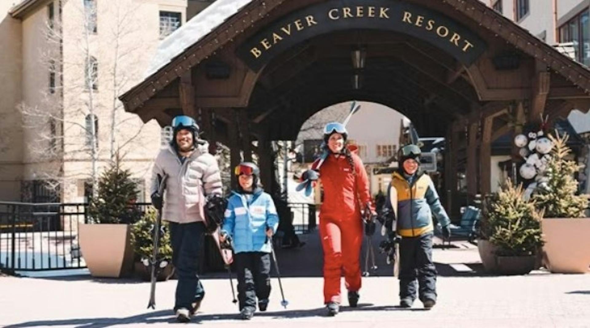 Parents and two kids in ski gear carrying skis standing outside Beaver Creek Resort