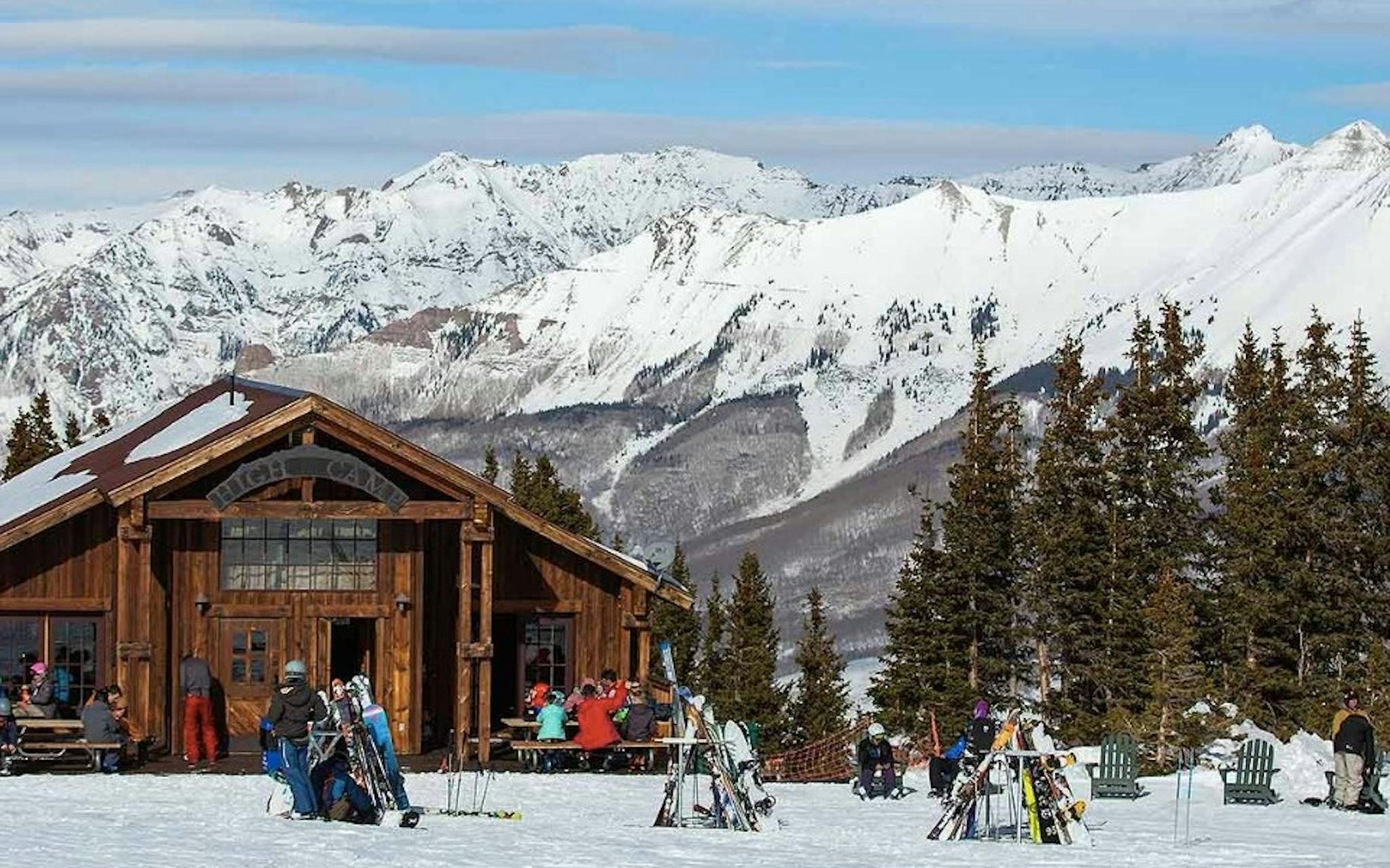 skiers sit at picnic tables outside the High Camp Warming Hut on a sunny day at Telluride