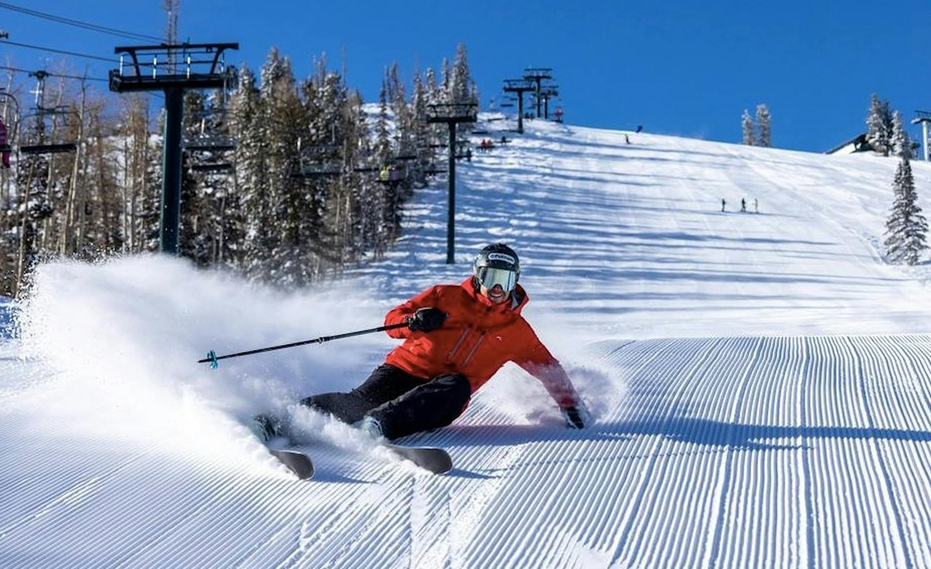 skier in orange jacket and shiny ski googles sprays snow on a freshly groomed slope at Deer Valley Resort