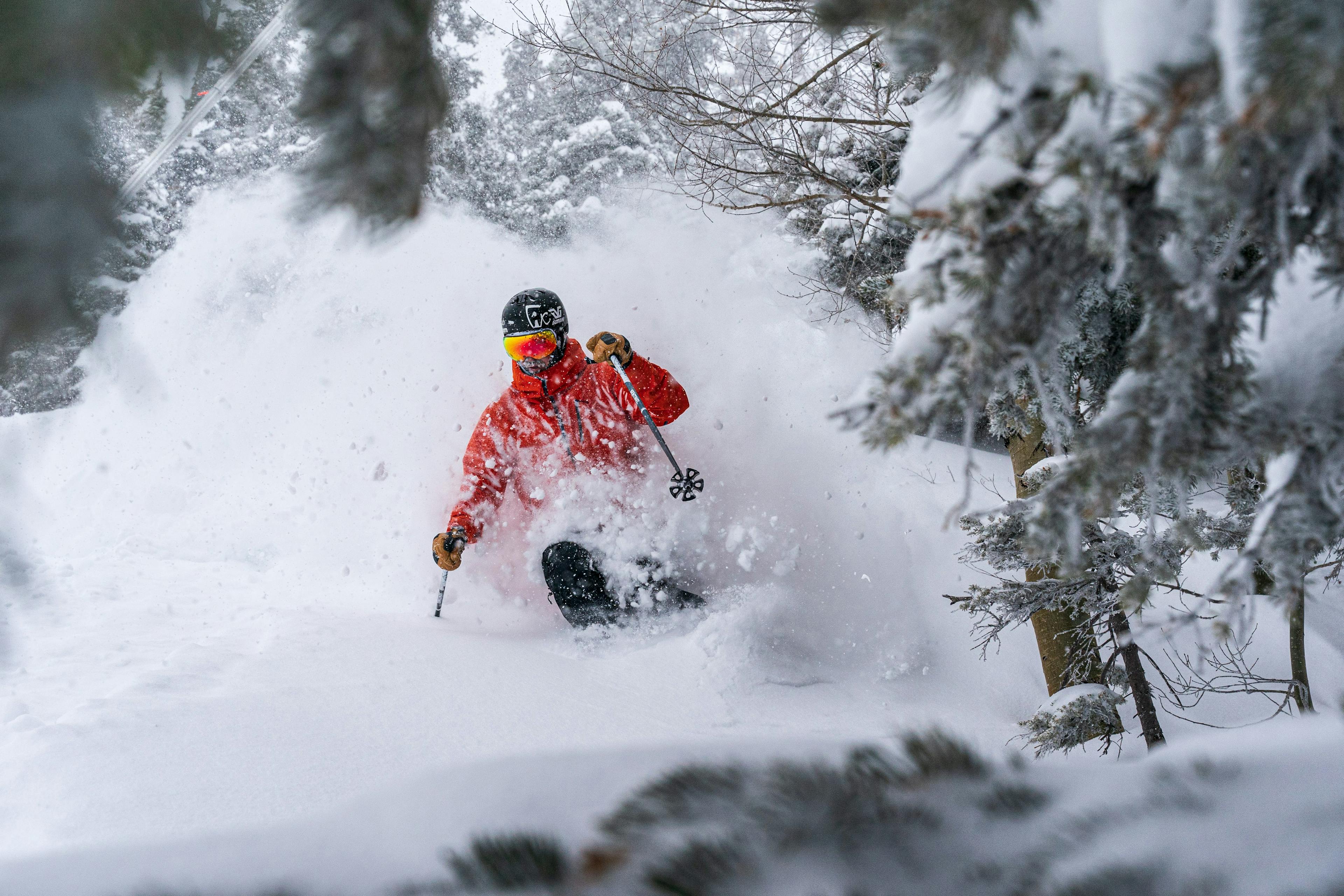 a skier in a red jacket blasts through deep powder in Taos