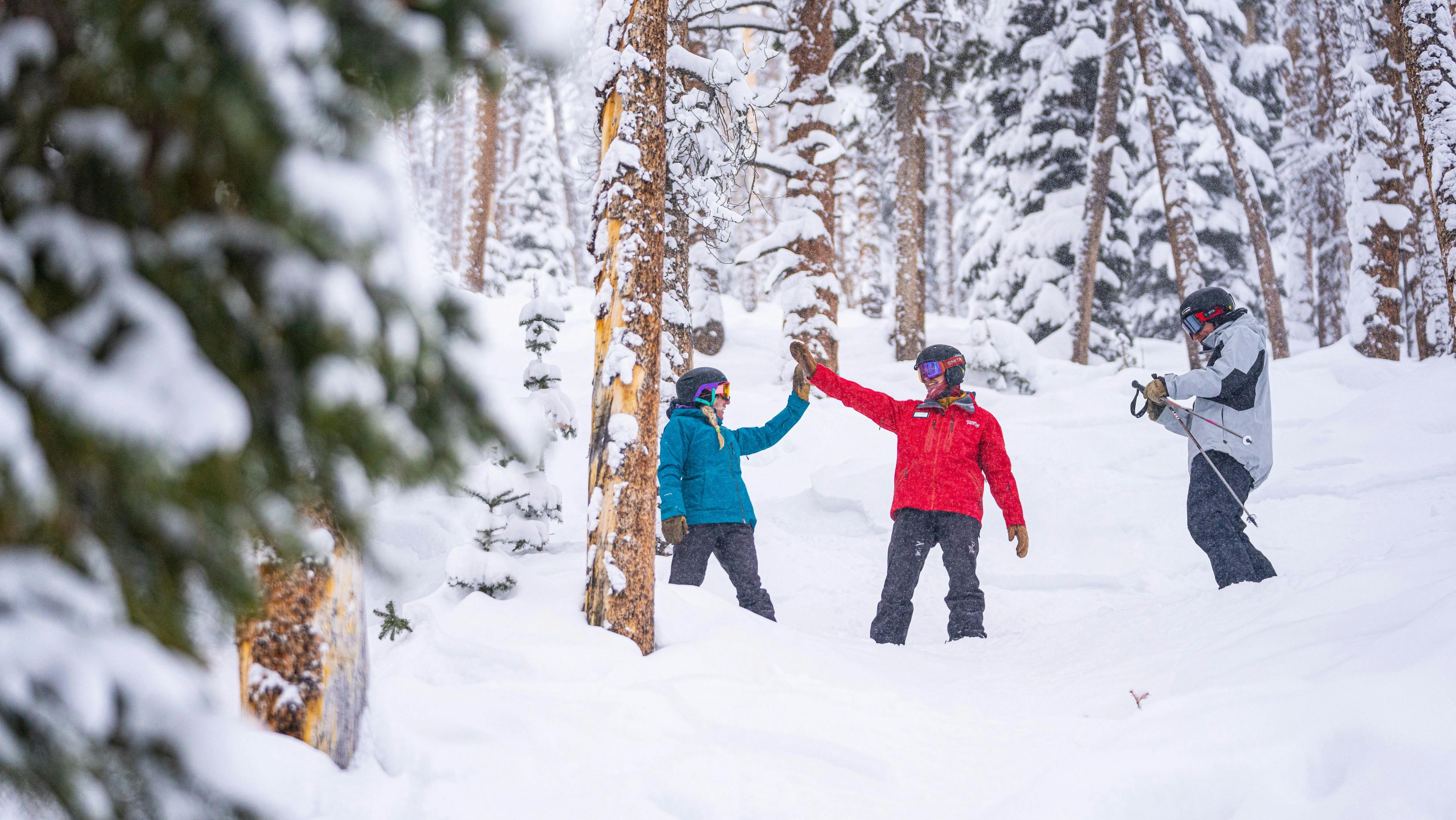 Ski guide high-fives a snowboarder on a snowy slope