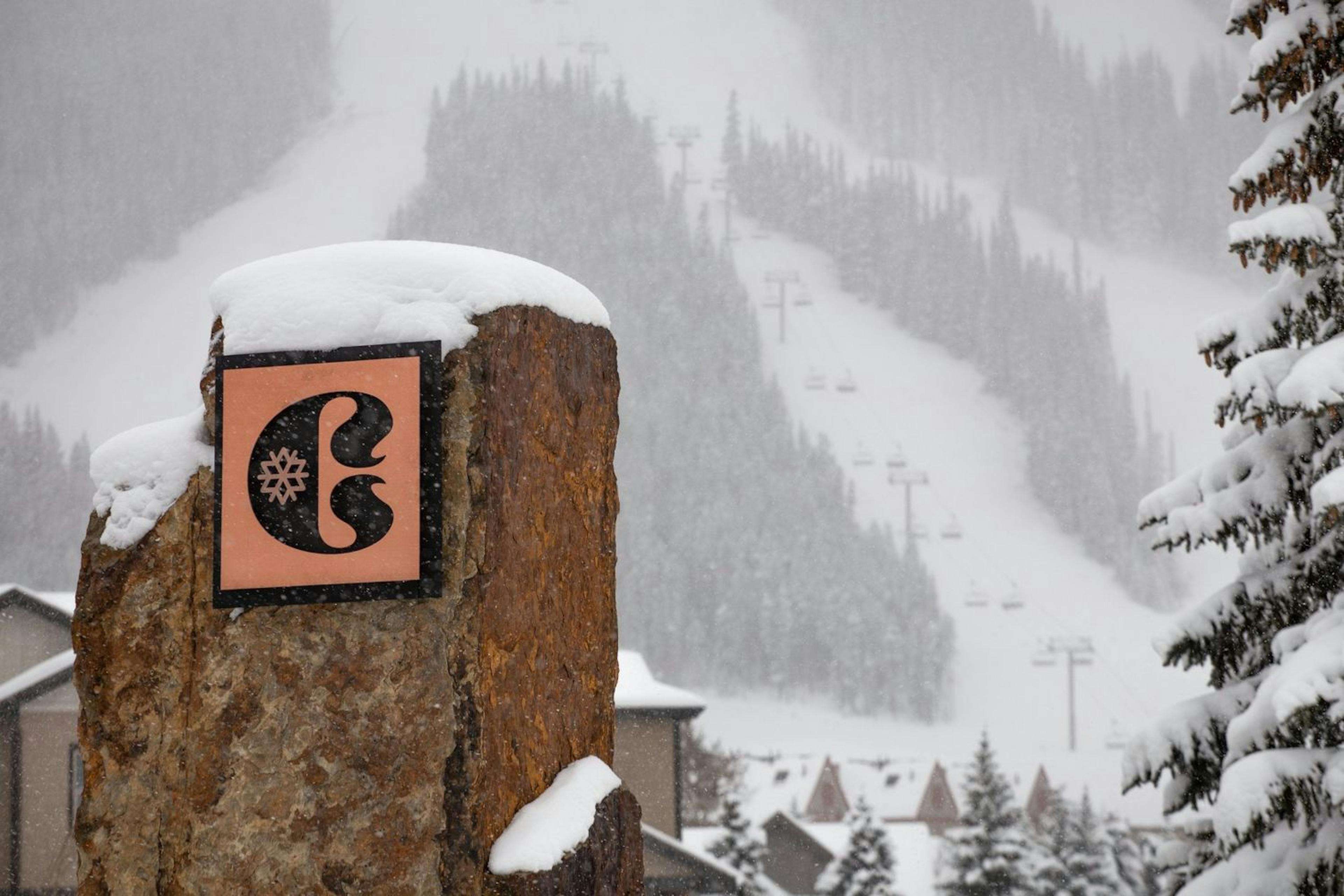  A snowy scene with a rock sign and a ski slope in the Copper Mountain Resort