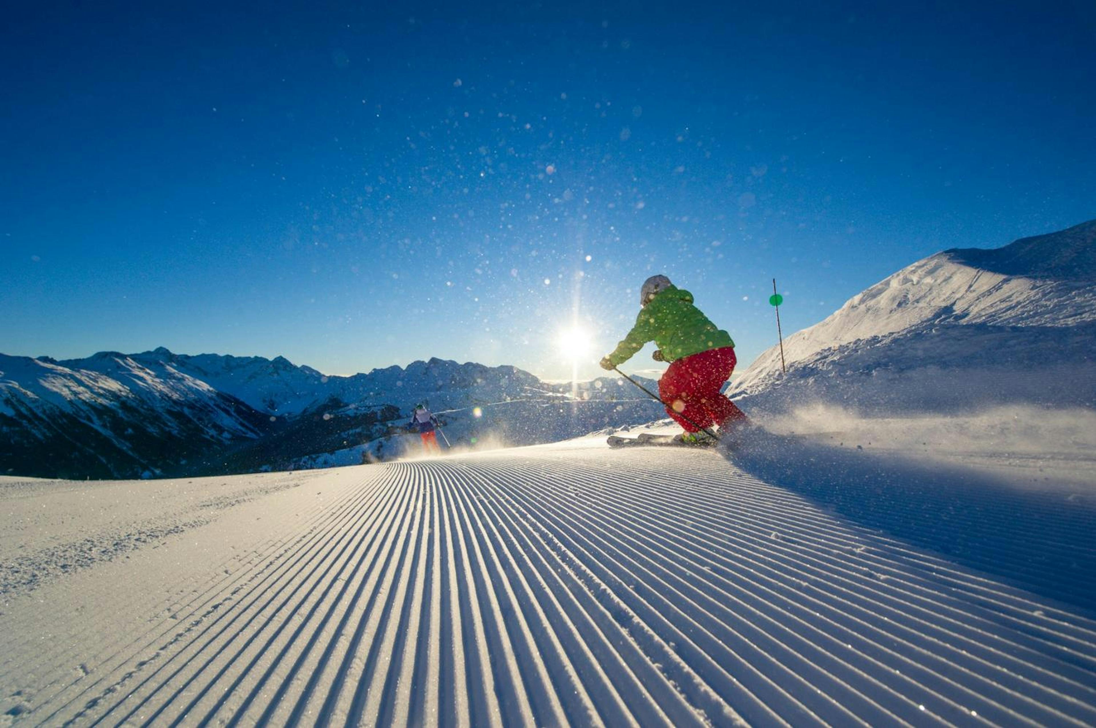 Skier of undiscernible gender in lime green ski jacket and pink ski trousers skiing first tracks at Whistler Blackcomb in British Columbia, Canada.