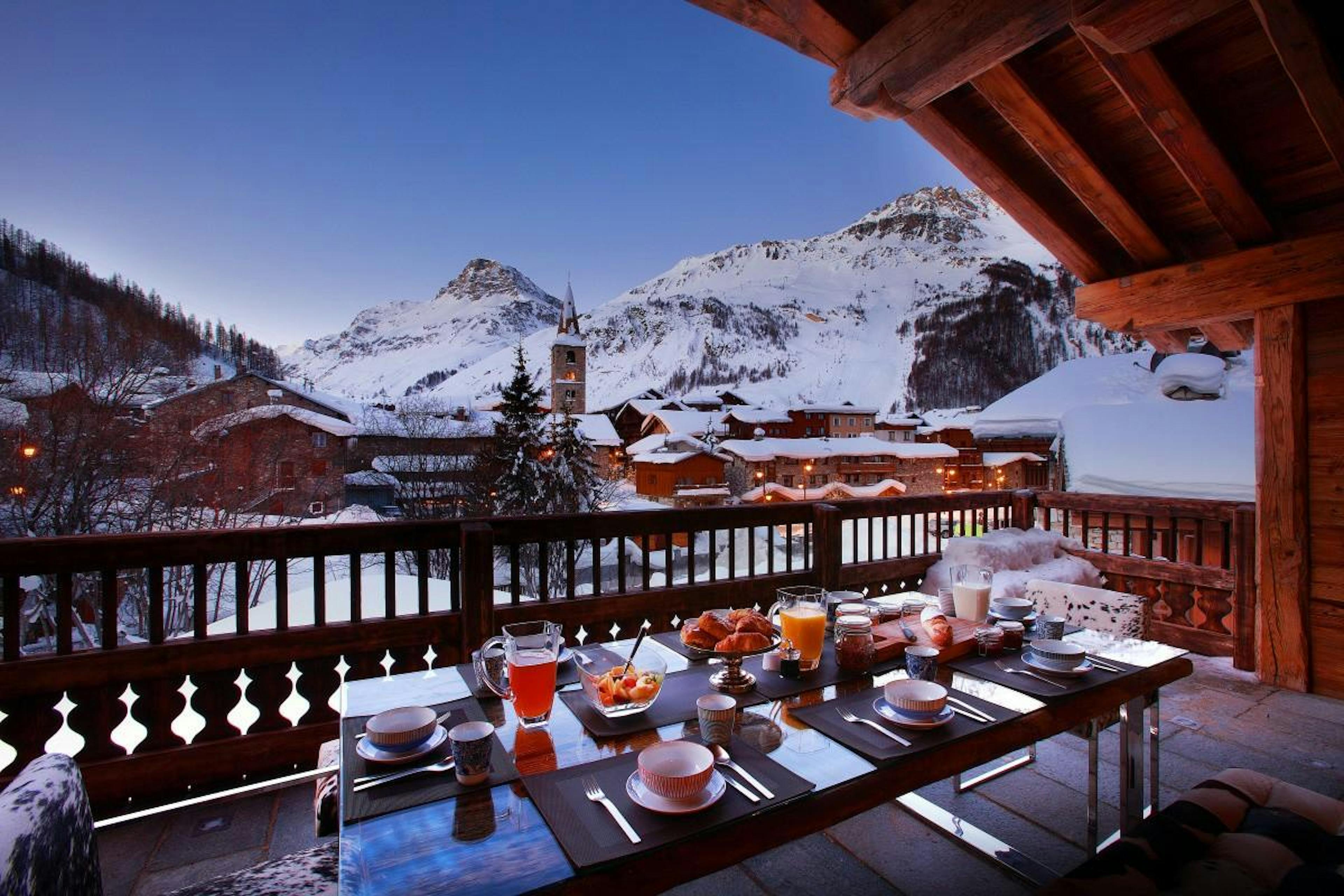 A table set on a balcony with fruit, pastries, and drinks in Val d'Isère.