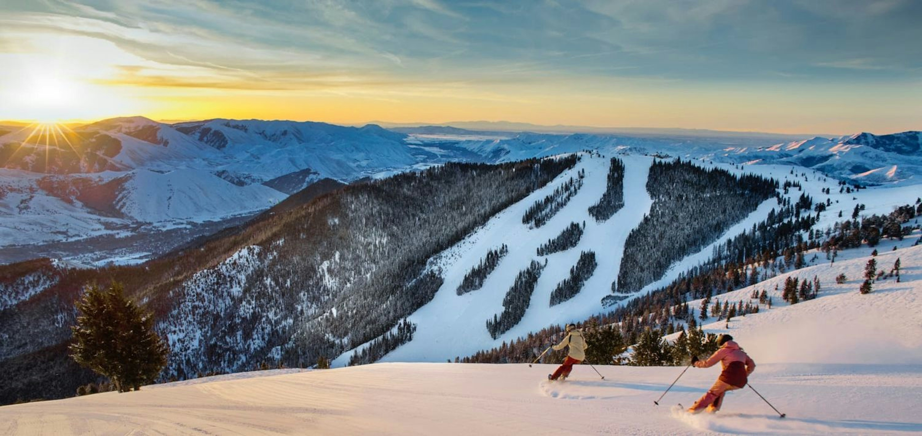 Two skiers skiing in Sun Valley with a shot of the sun setting in the back