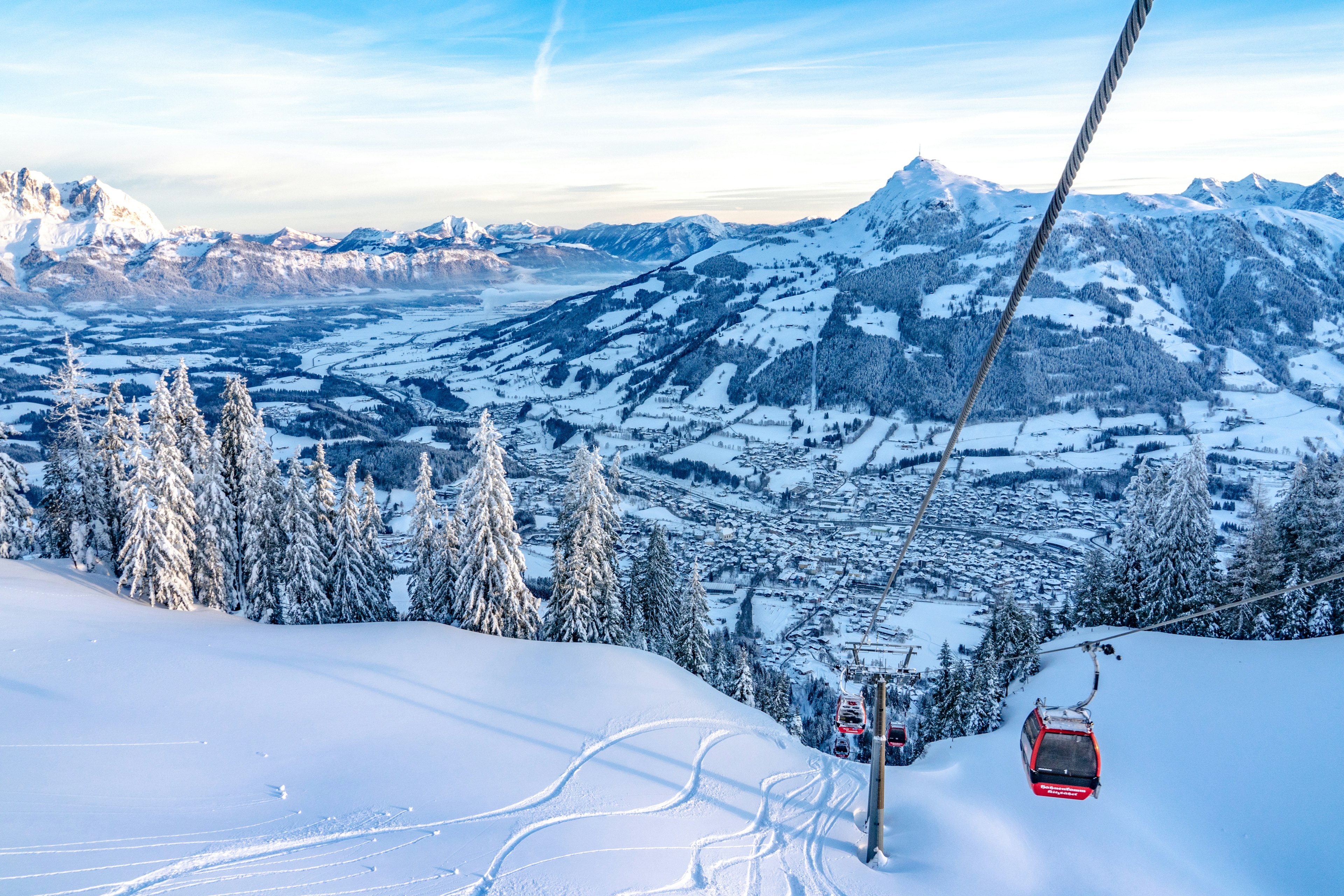 A scenic ski lift in snowy Austria, surrounded by tall trees and majestic mountains under a clear blue sky.