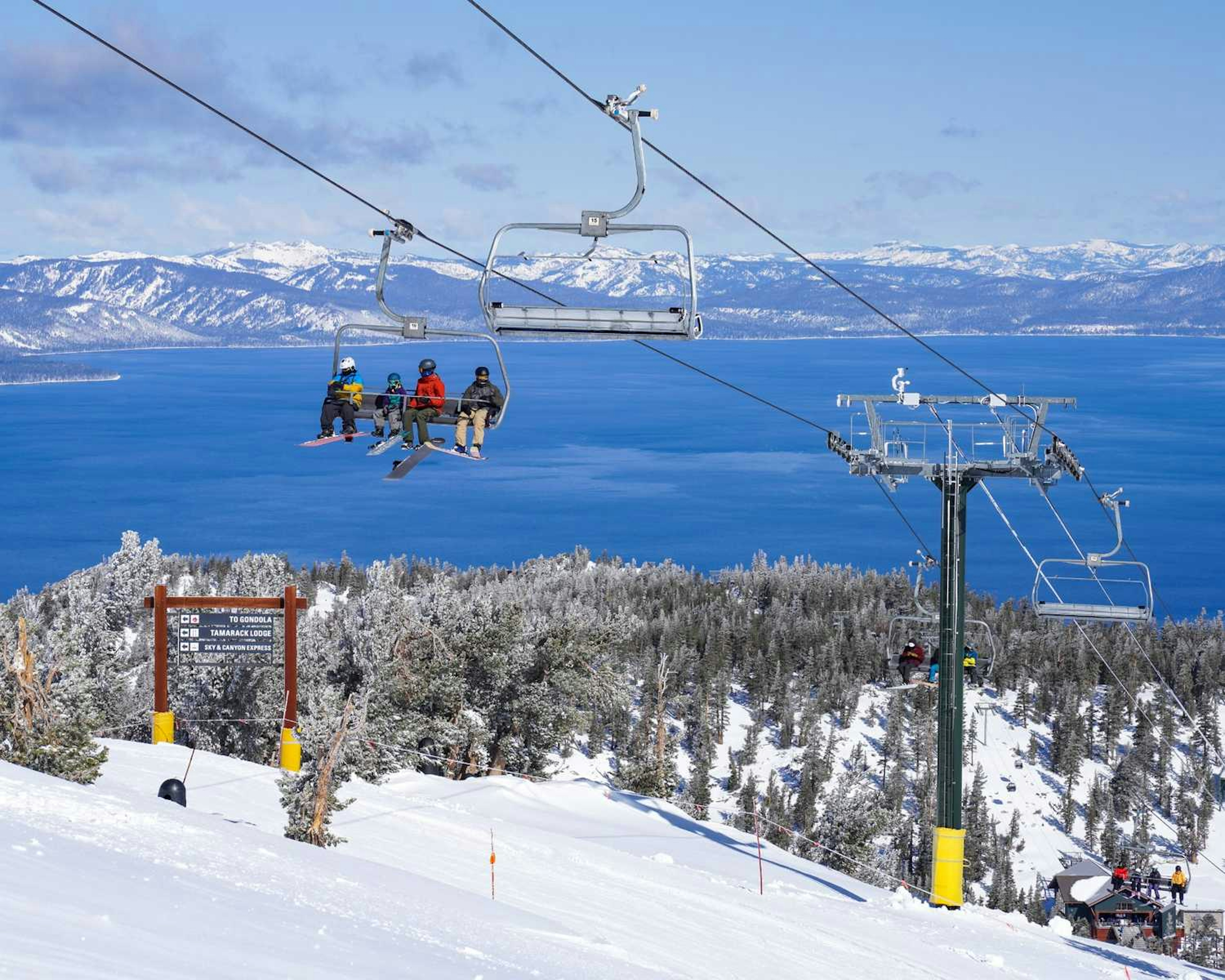 Skiers sitting on the lift in front of Lake Tahoe.