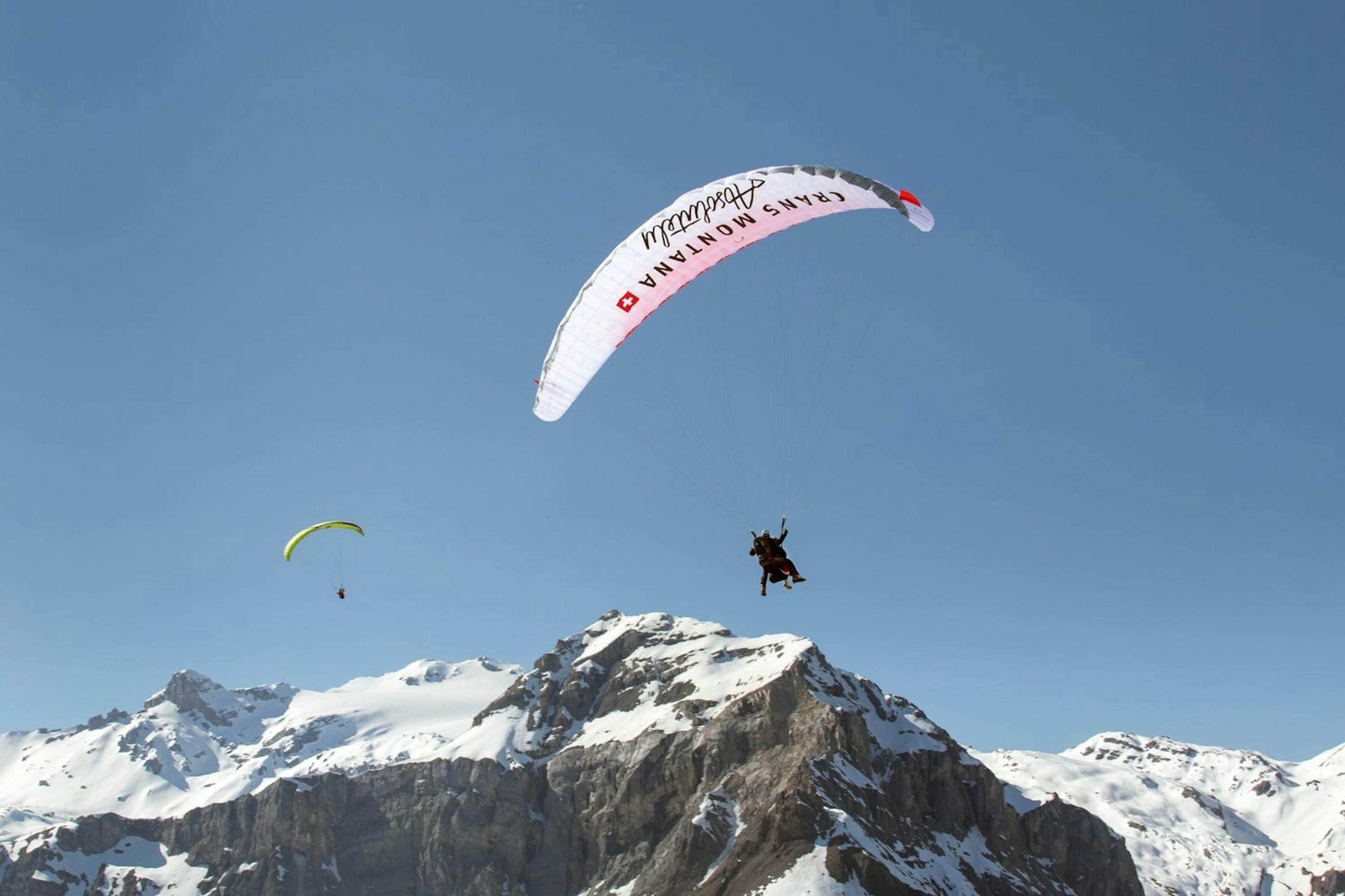 Adventurers paragliding over snowcapped mountains in Crans-Montana. 