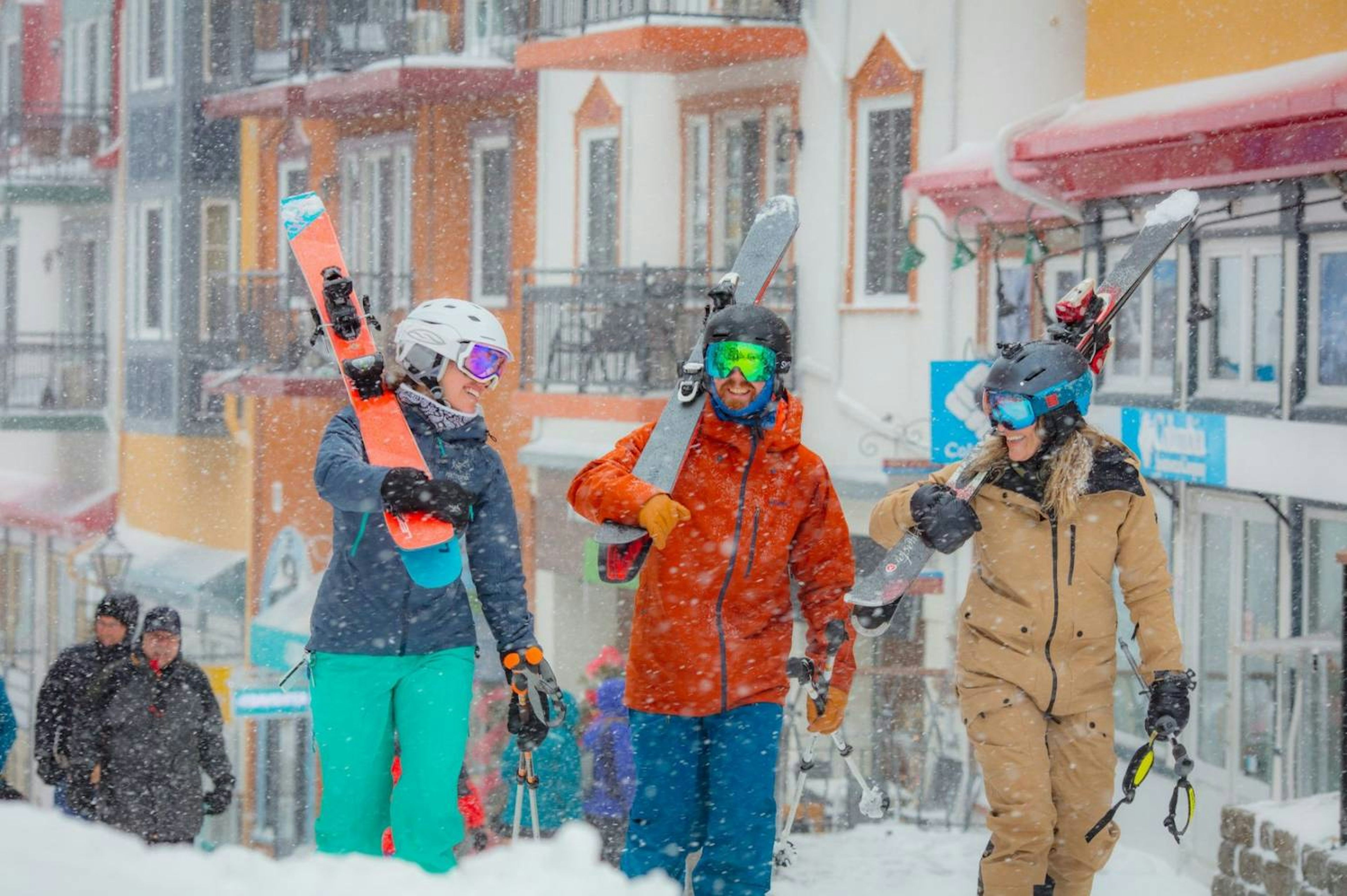 Three skiers stroll down a snowy street, surrounded by white snow and winter scenery, enjoying a chilly day outdoors.