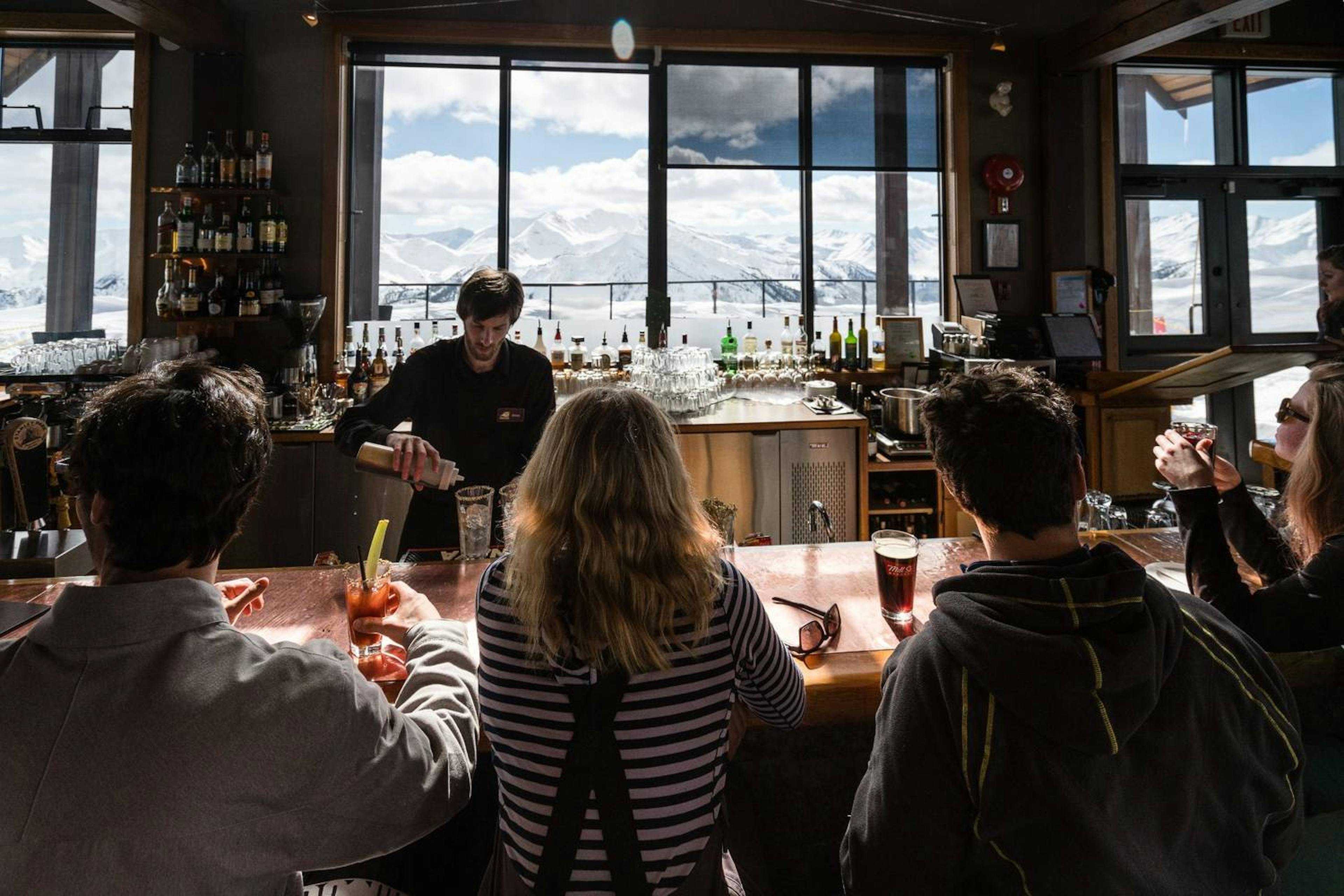 A group of friends enjoying drinks at a bar with stunning mountain views of Kicking Horse in the background.