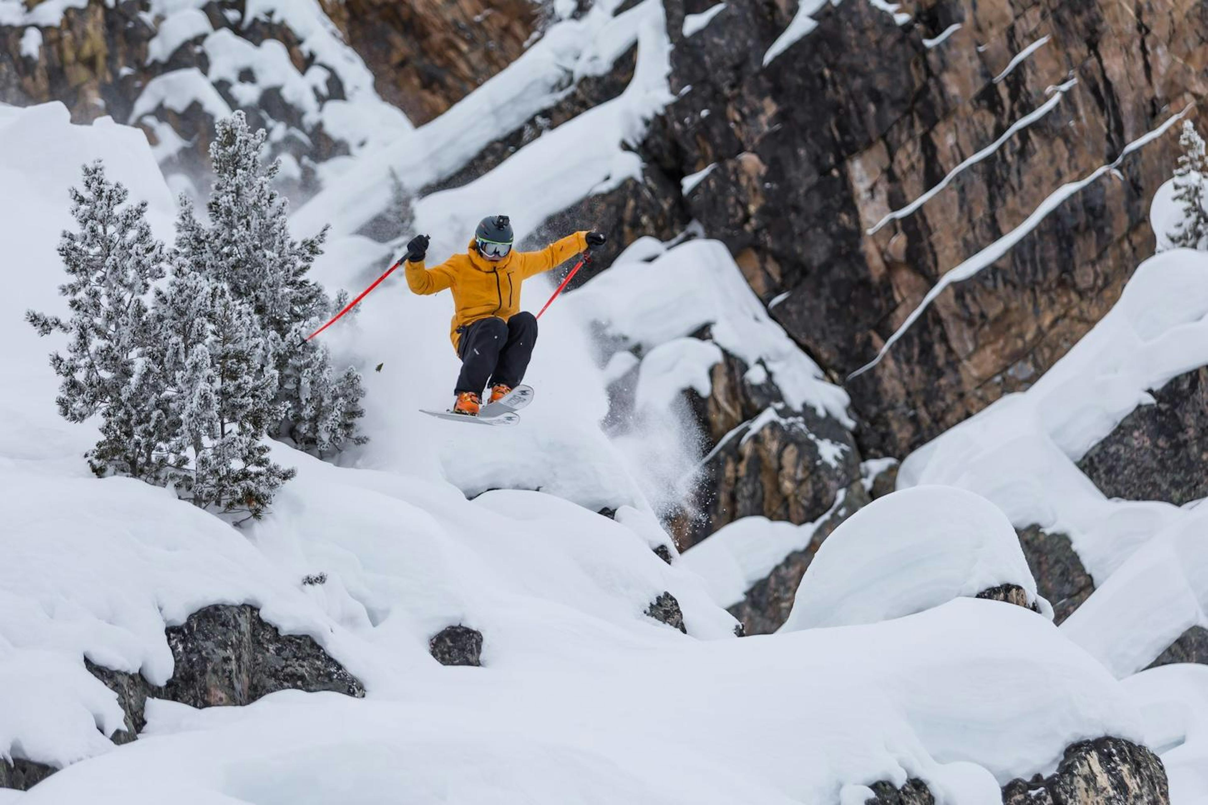 A man in a bright yellow jacket jumps off the snowy slopes of Kicking Horse Mountain.