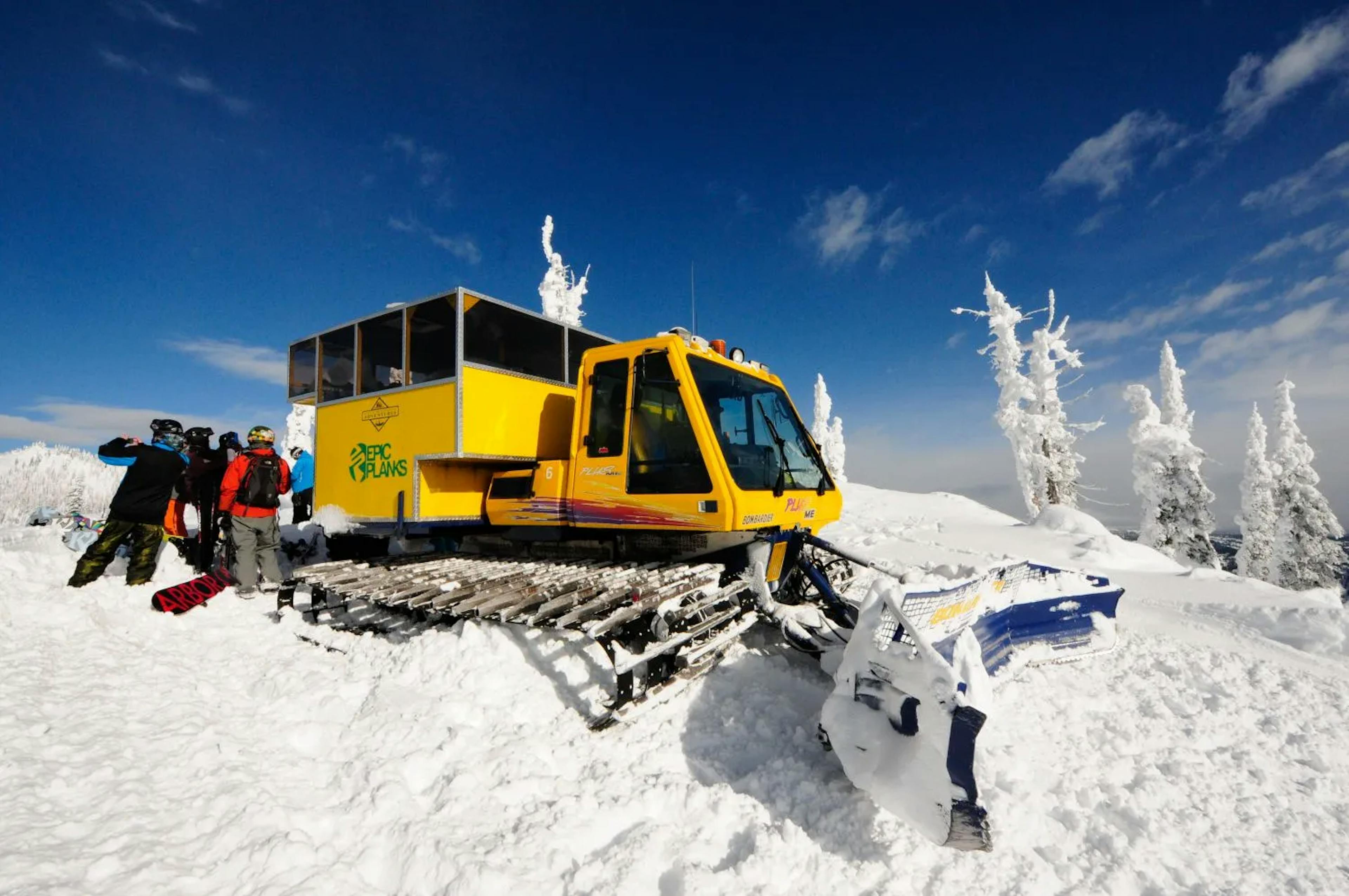 A group of skiers alongside a snowcat. 