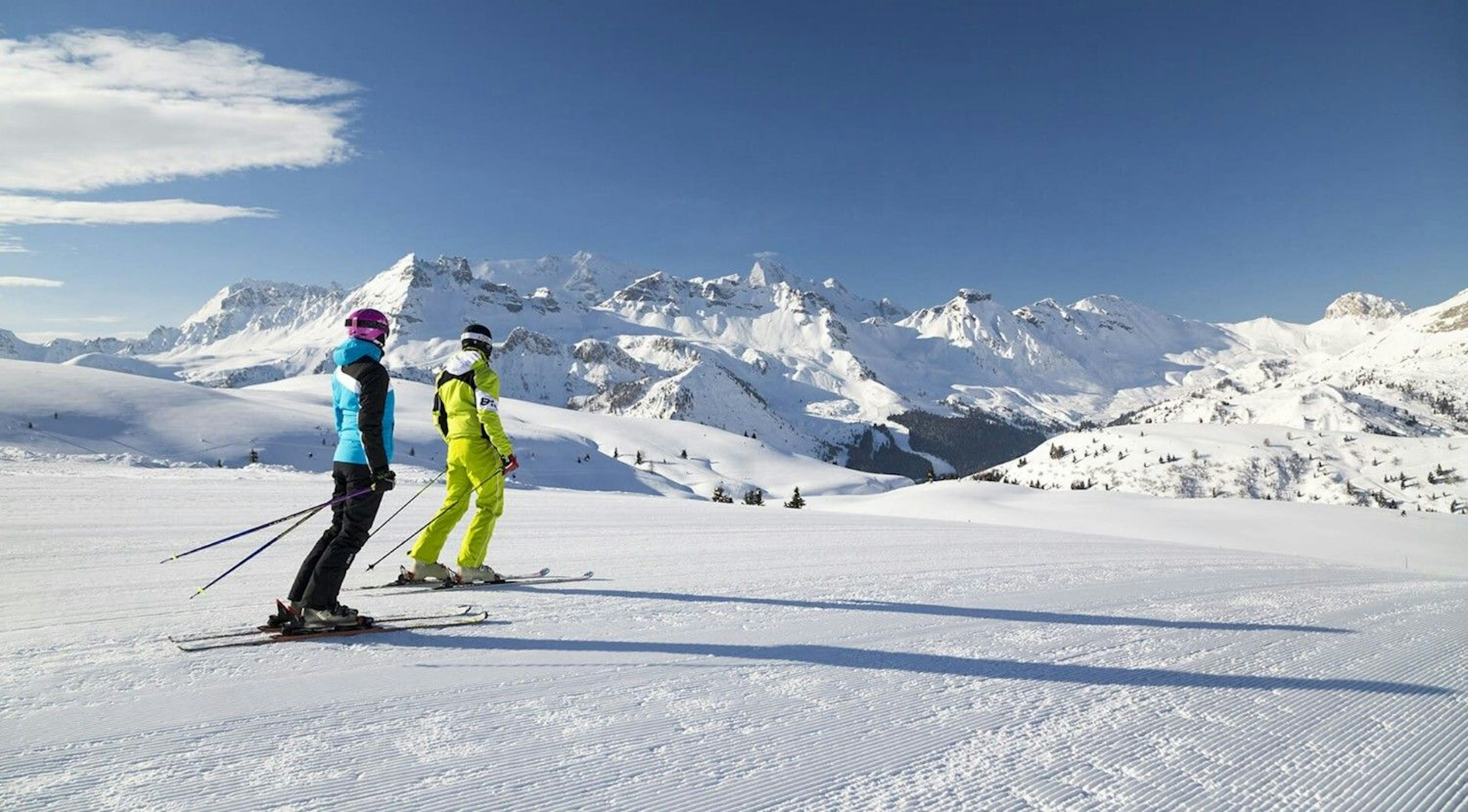 Two skiers look out at endless mountain peaks covered in snow in Arabba Marmolada in Italy.