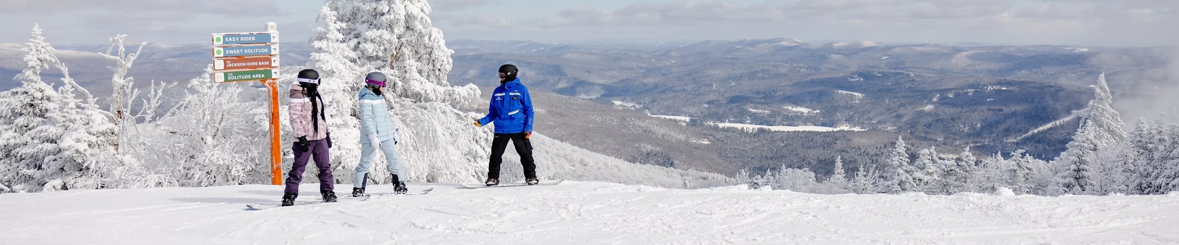 Three skiers stand proudly on a snowy summit at Okemo