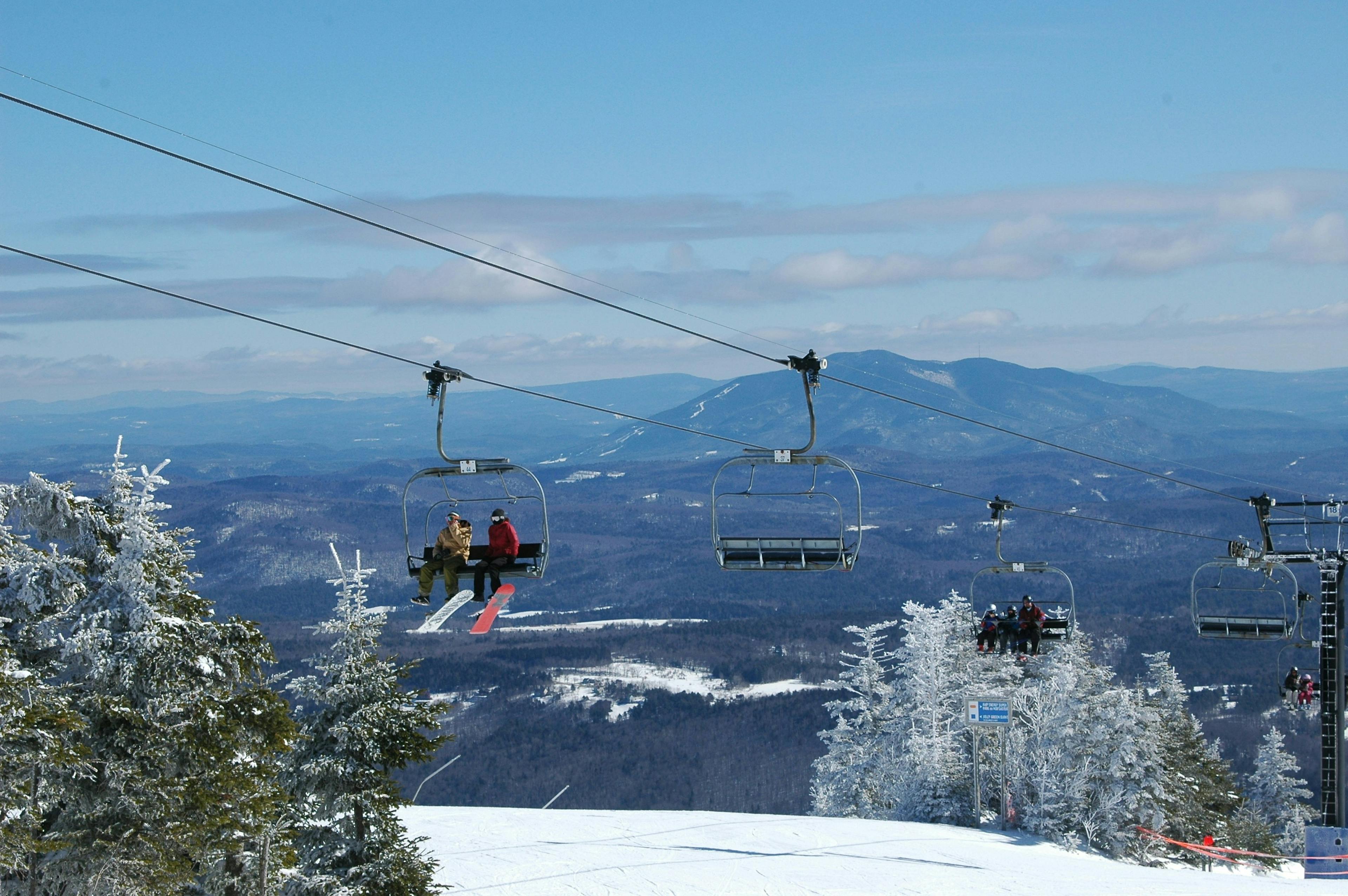 Two friends ride a ski lift at Okemo, taking in the beautiful snowy scenery as they ascend the mountain.