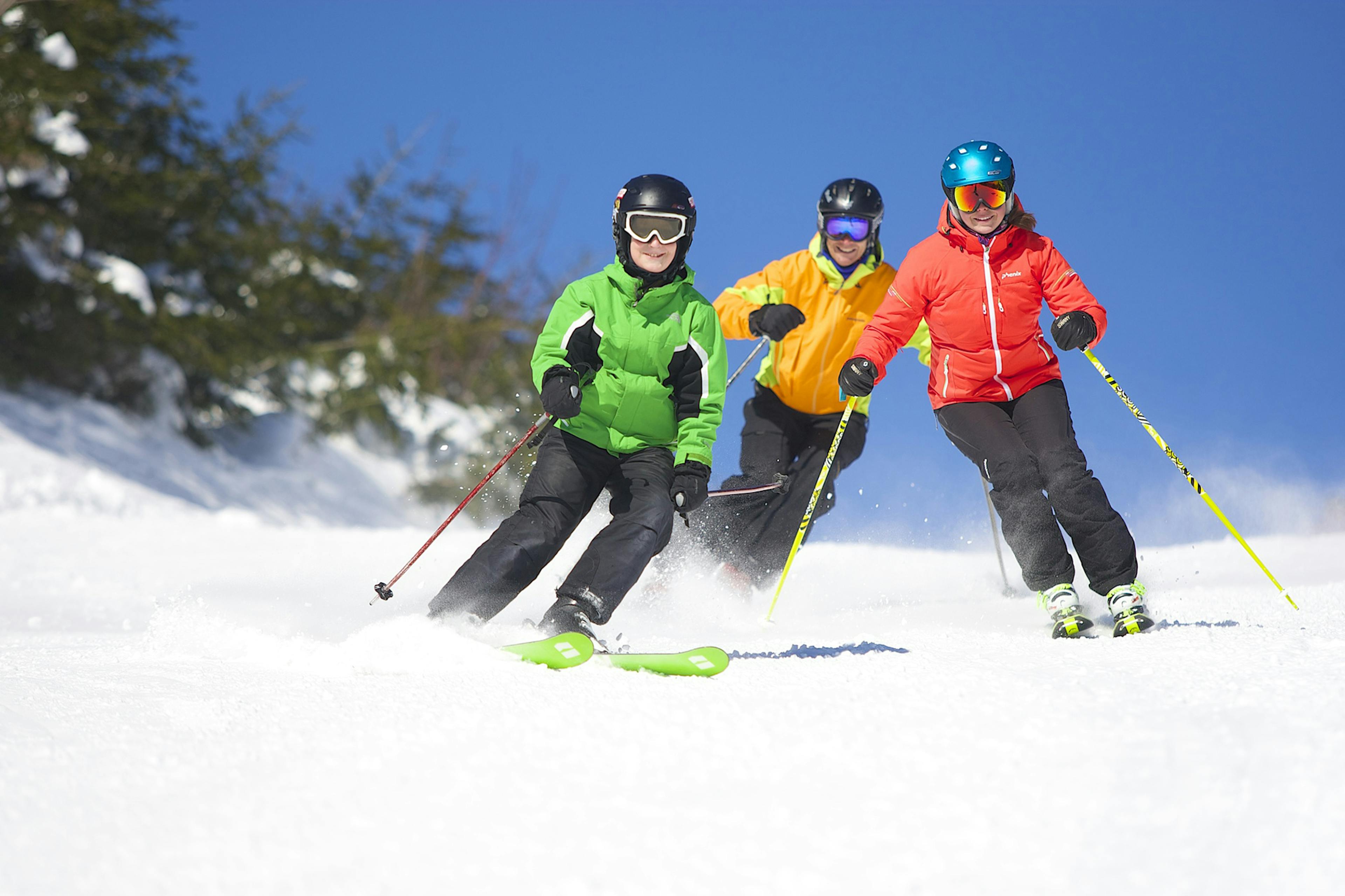 Three friends ski down a snowy slope at Okemo