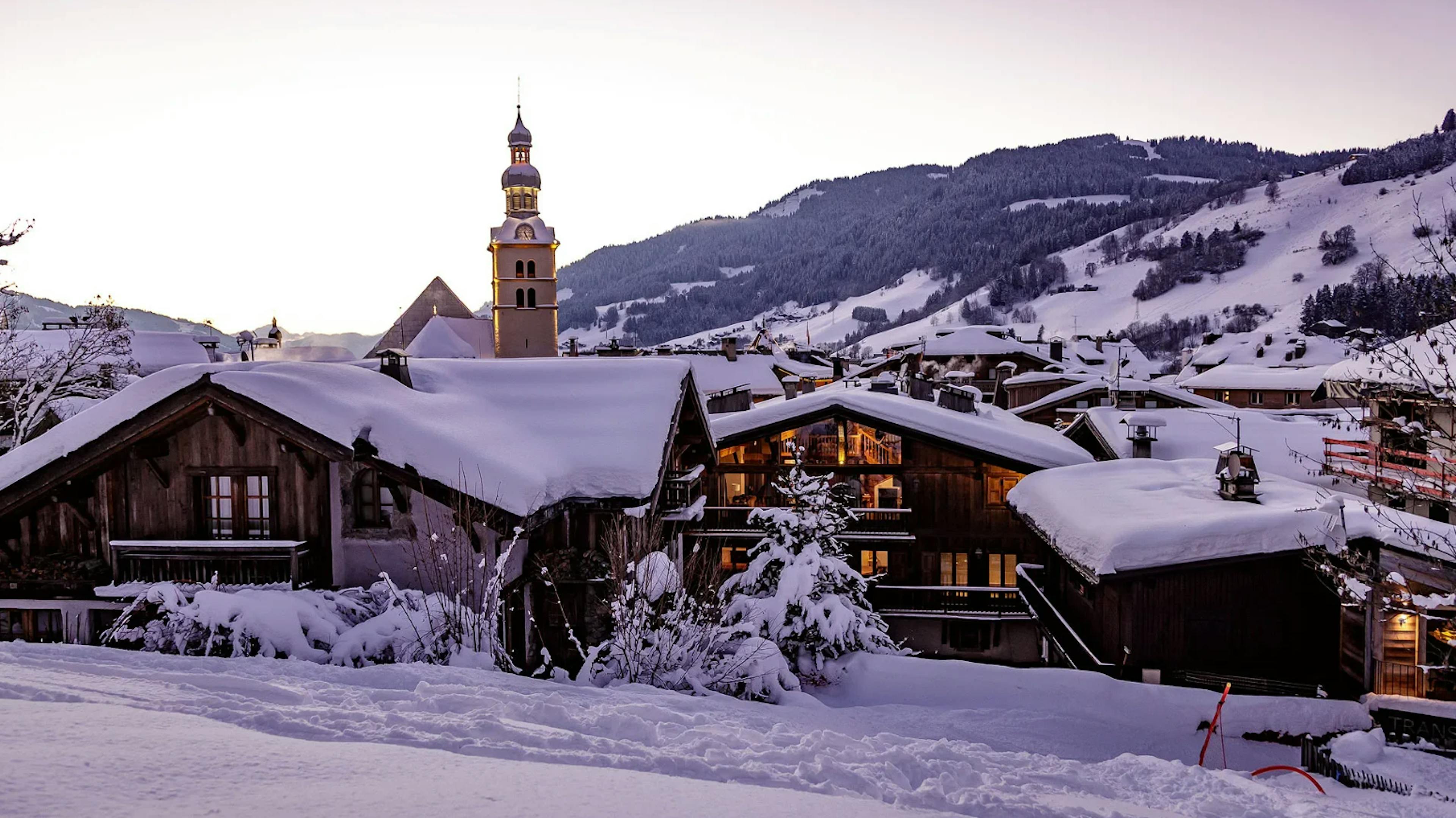 megeve france at twilight with all chalets covered in snow and a church in the background

