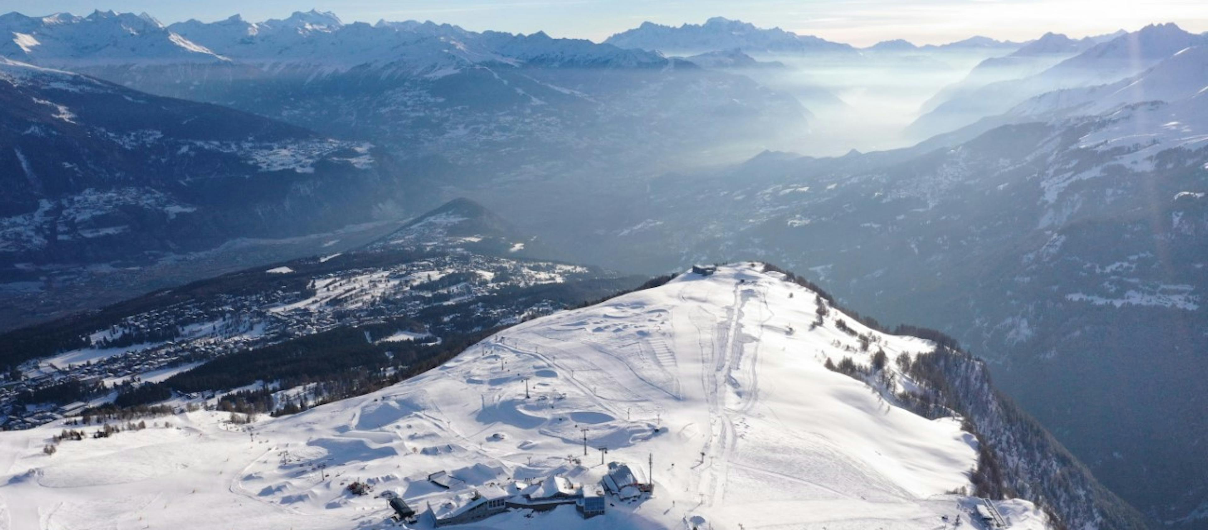 birds eye view of crans montana ski resort with sun glistening off the snow and large mountain peaks in the background

