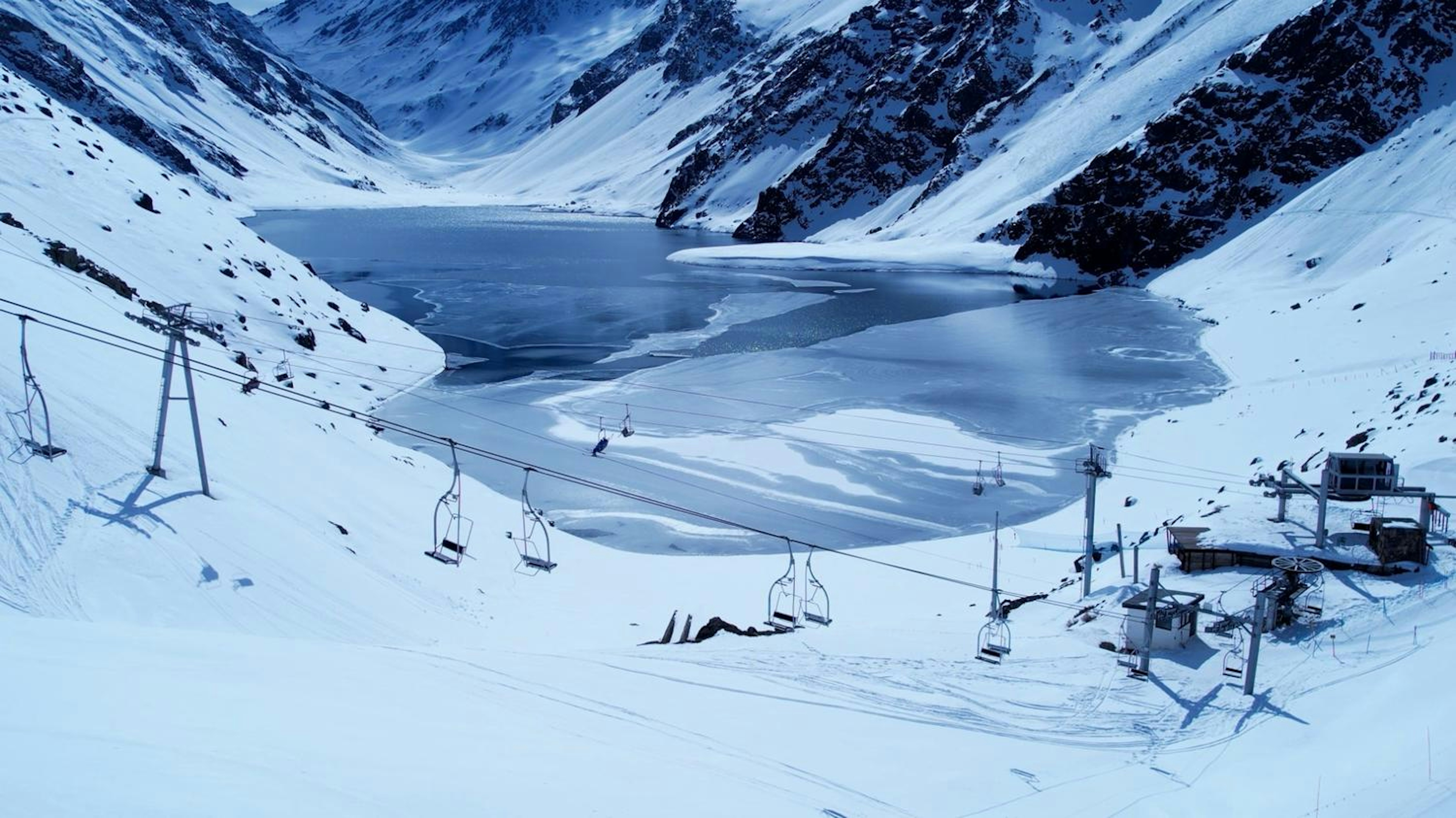 A ski lift ascends a snowy mountain in Chile, surrounded by pristine white slopes and a clear blue sky.