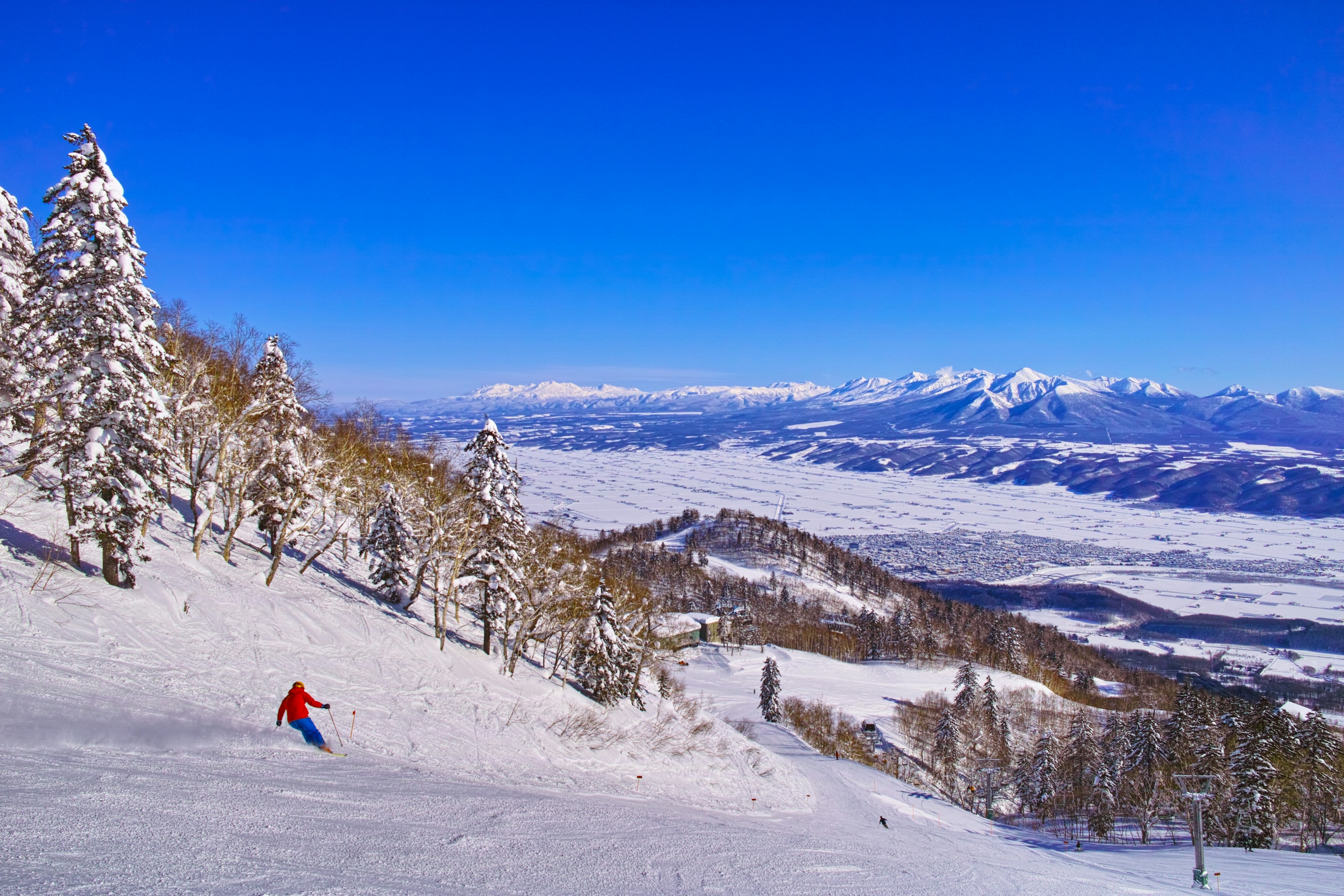 furano ski resort with a skier in red jacket going down the groomed run