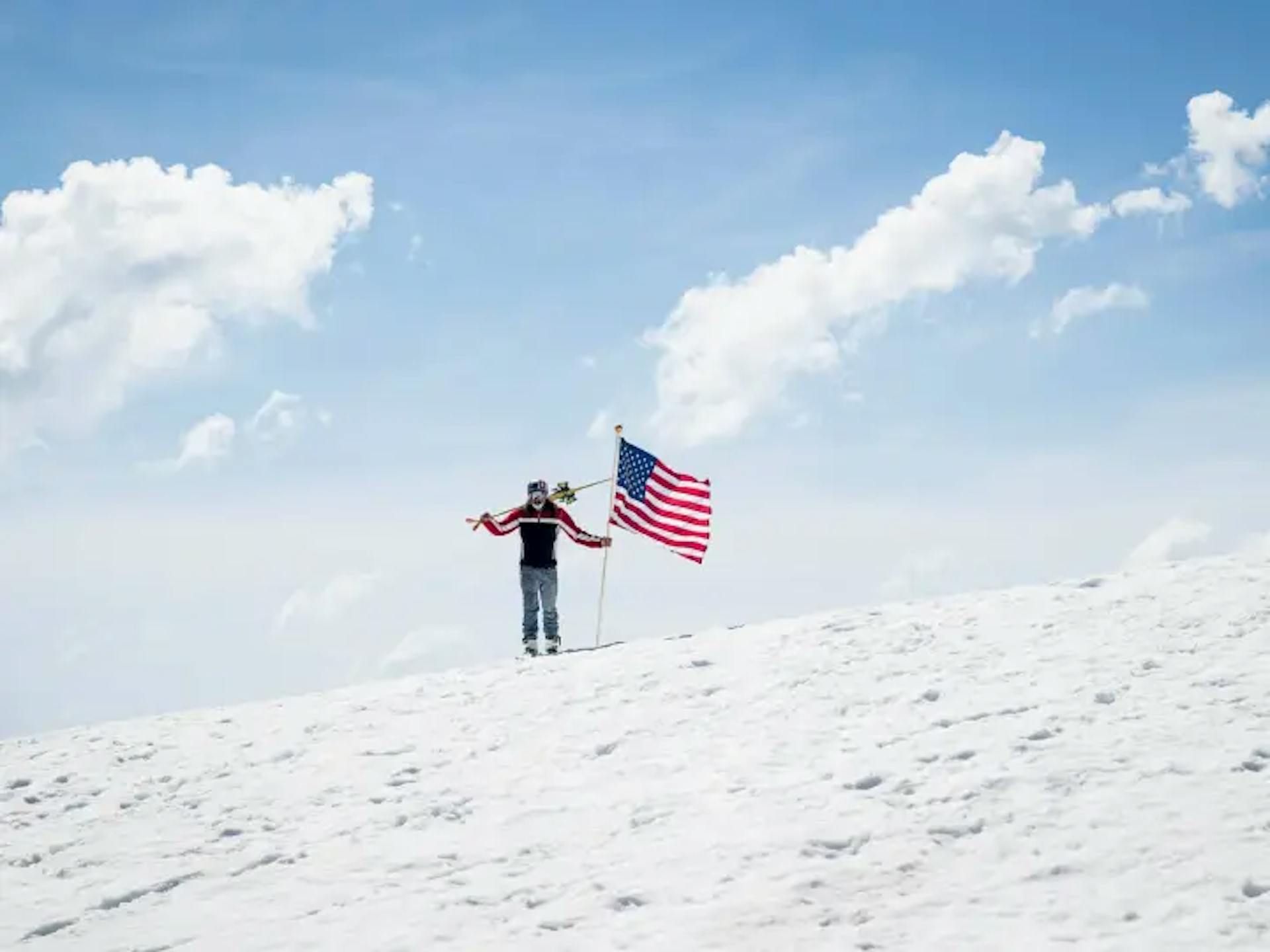 A skier holding the American flag on the summit of a mountain