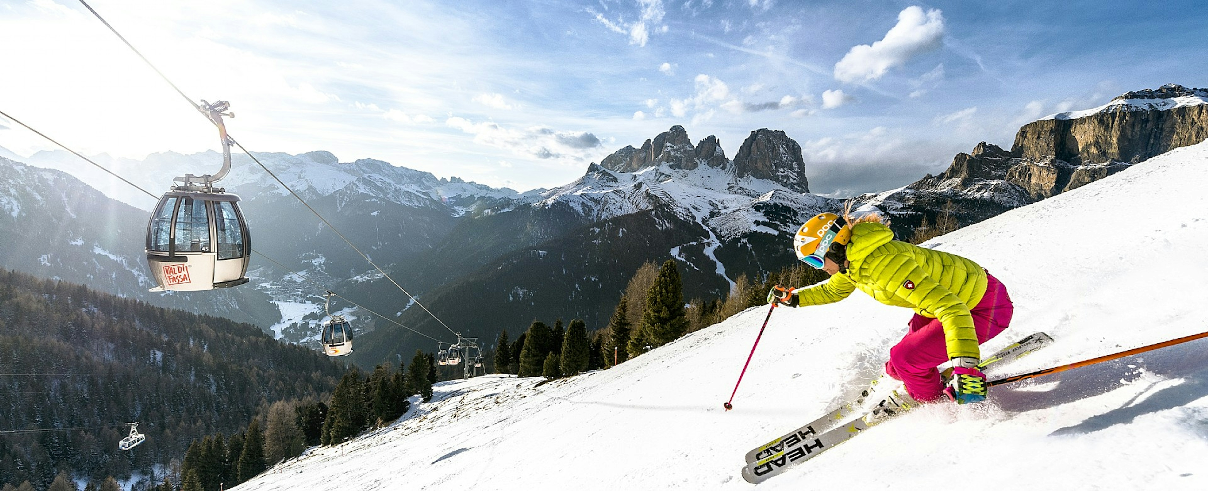 Female skier in pink ski trousers and yellow ski jacket skiing the slopes of Val di Fassa in Italy