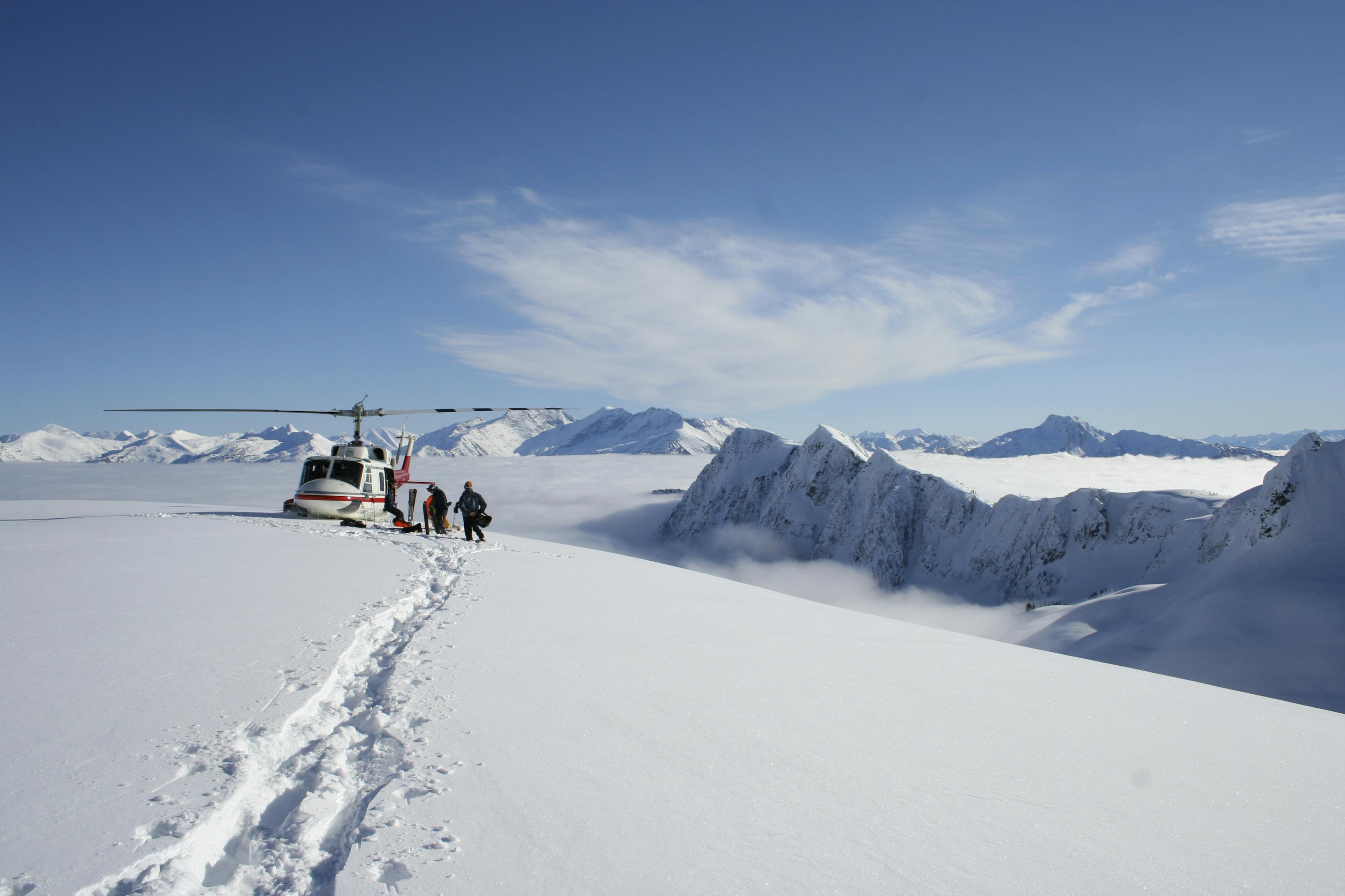  A helicopter is parked on a mountain, surrounded by rugged terrain and clear blue skies.