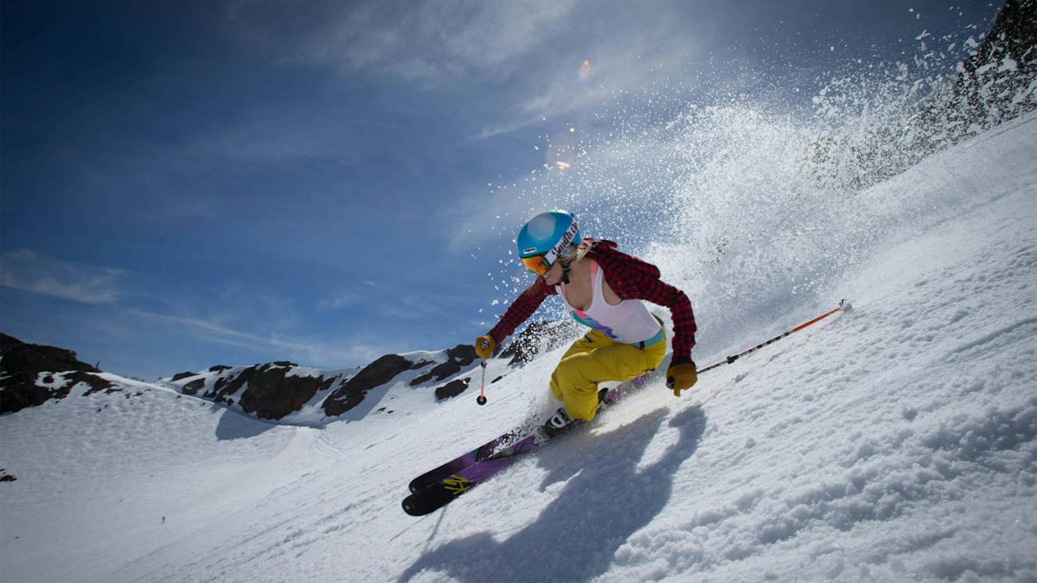 Female skier in yellow ski pants hits the slopes in the month of May at Palisades Tahoe (Squaw Valley) in California, USA.
