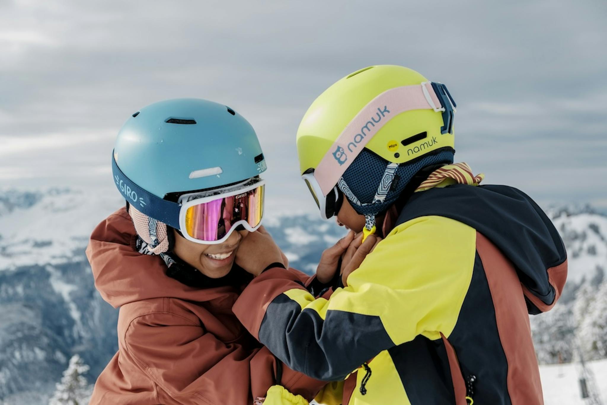 Two kids dressed in colorful jackets and hats, happily enjoying a snowy day together.