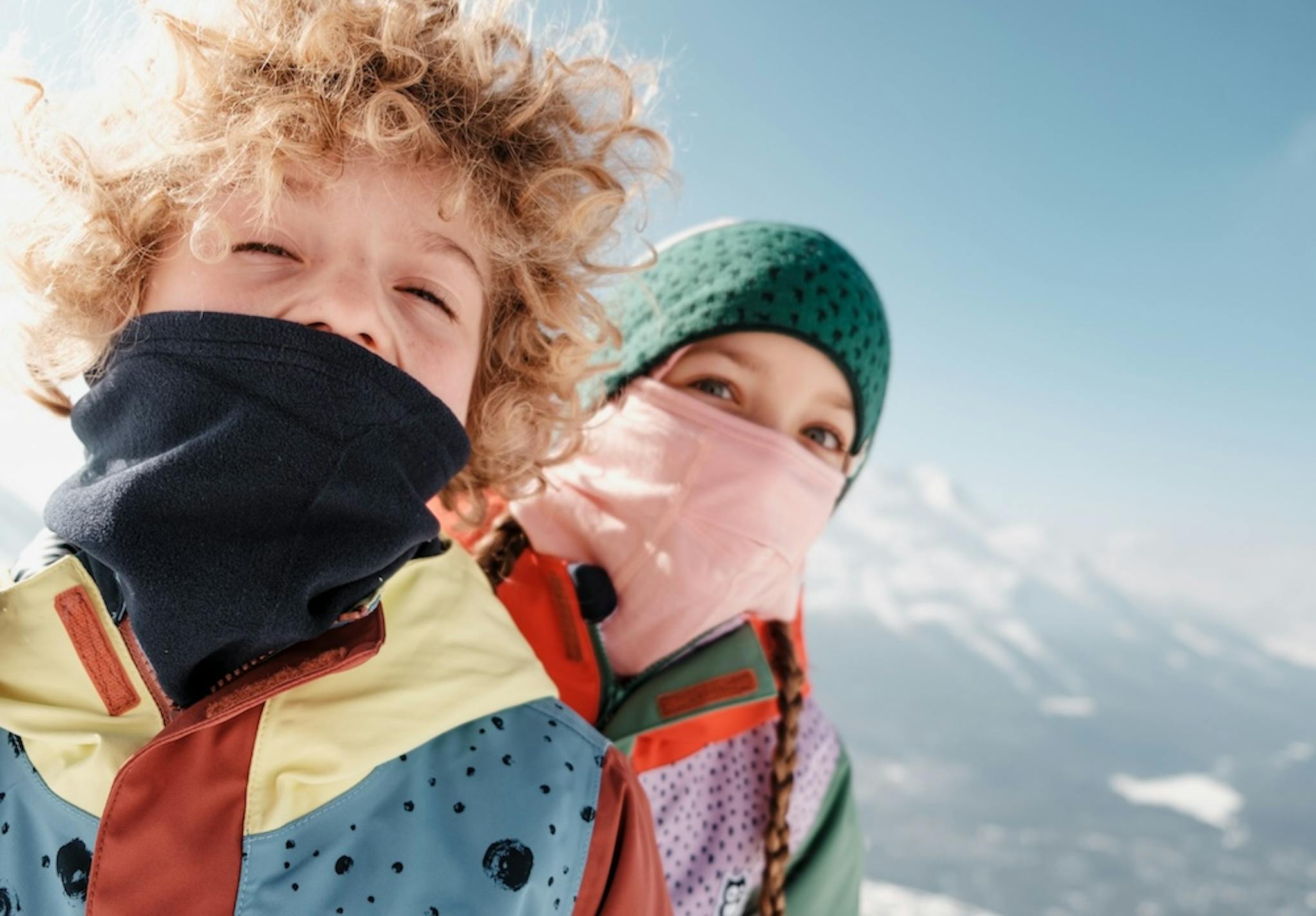 Two cheerful children in vibrant jackets and hats, having fun in a snowy landscape.