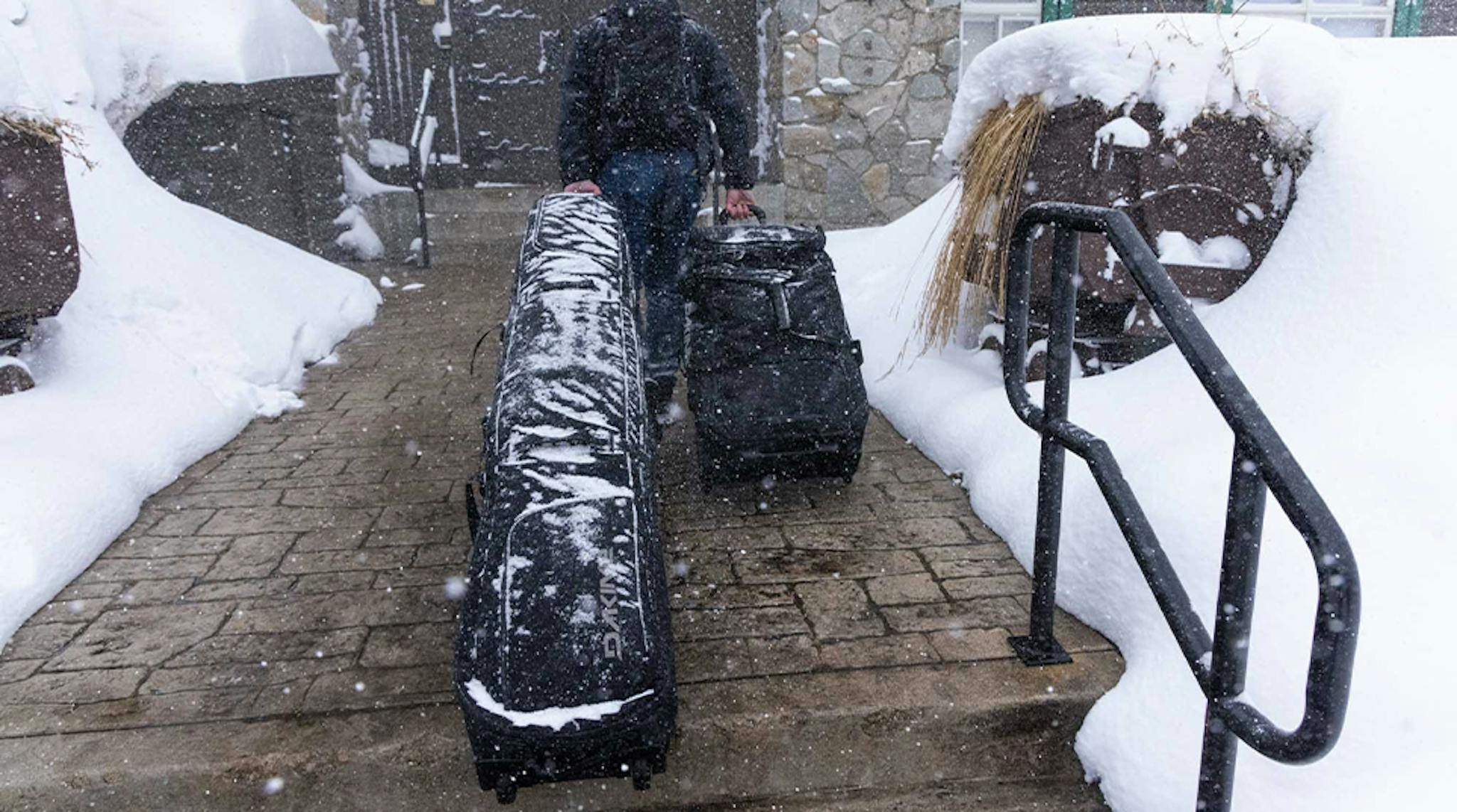 A man walks down a snowy path, carrying a suitcase