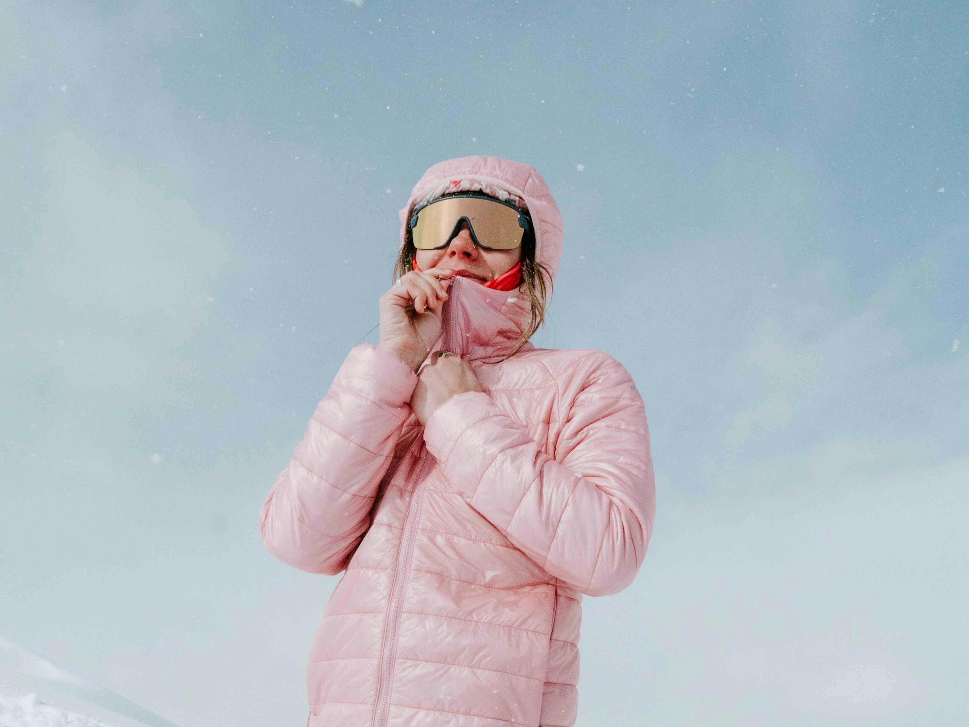 A woman dressed in bright pink snow gear strikes a fun pose for a photo against a snowy backdrop.