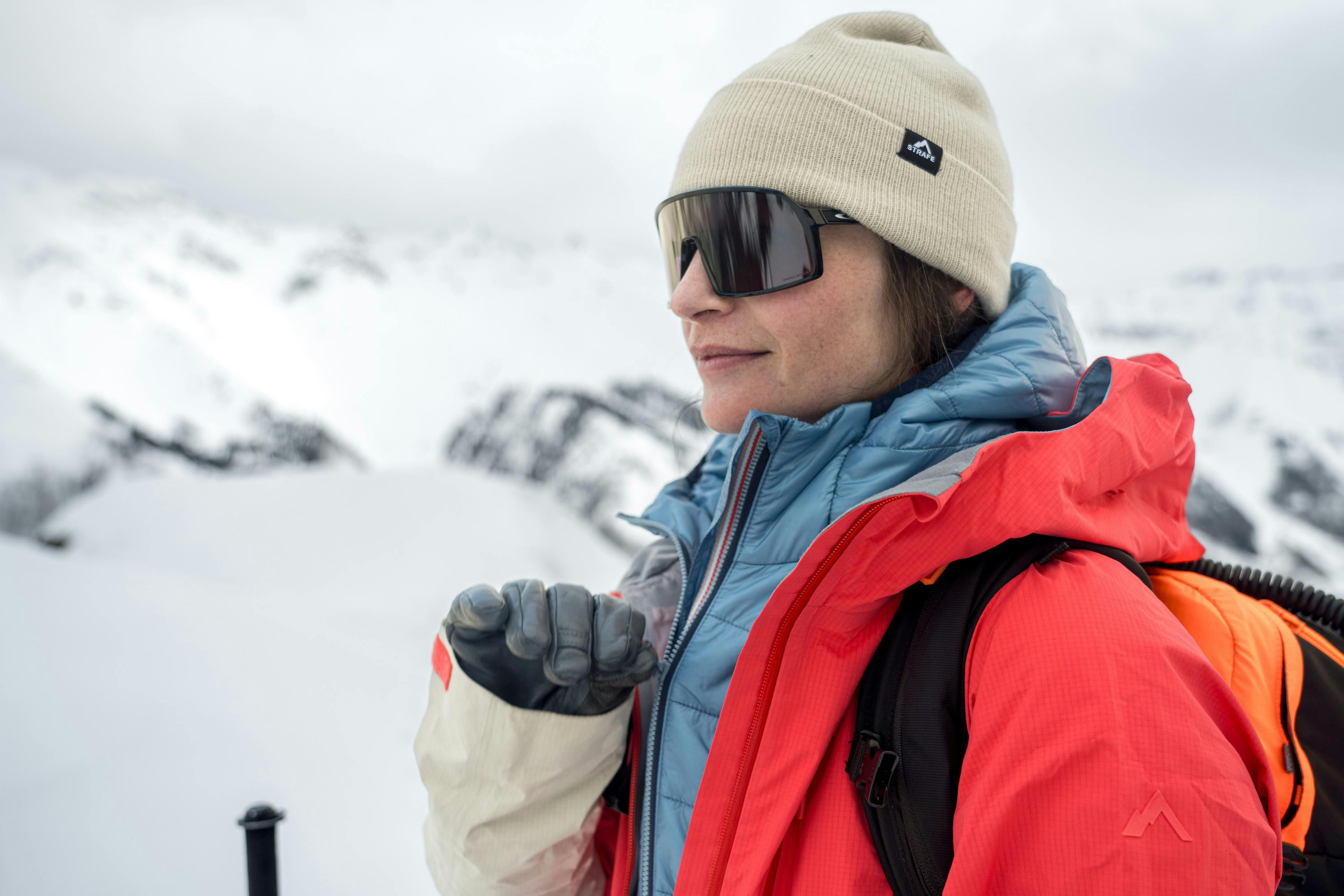 A woman wearing a red jacket and blue hat enjoys the snowy mountain scenery