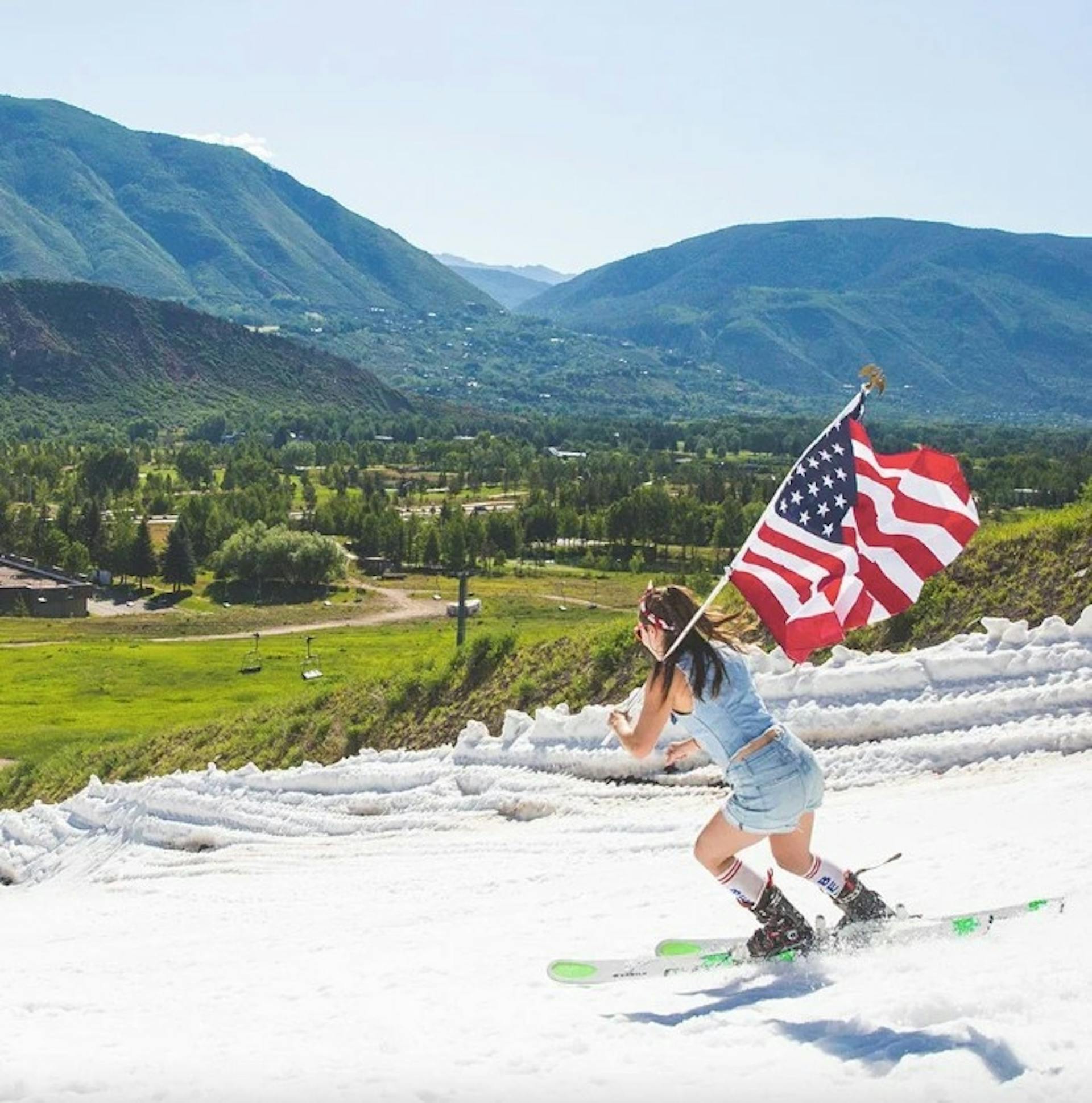 Woman wearing jean shorts and holding an American flag while skiing down the slopes at Aspen Ski Resort