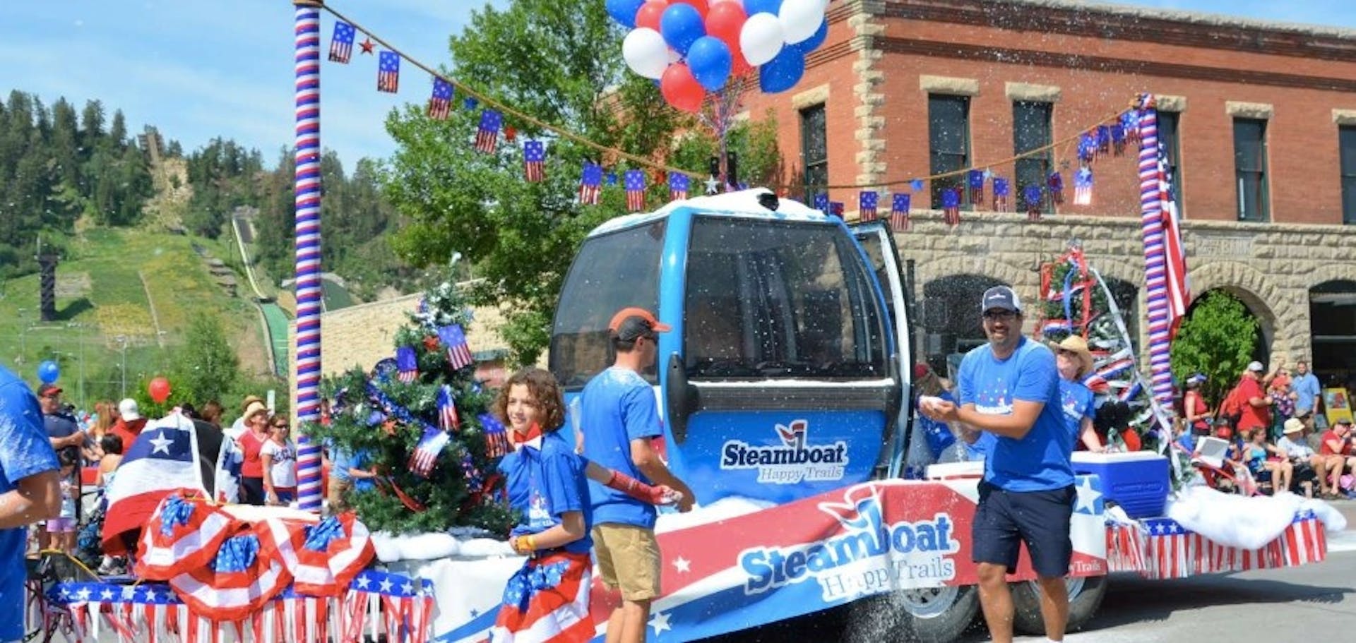 Participants walk in the Steamboat Springs 4th of July parade alongside a Steamboat Ski Resort Gondola float