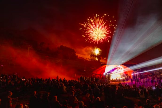 Fireworks burst over a crowd of people in front of a stage with live music at the Crested Butte 4th of July Celebration