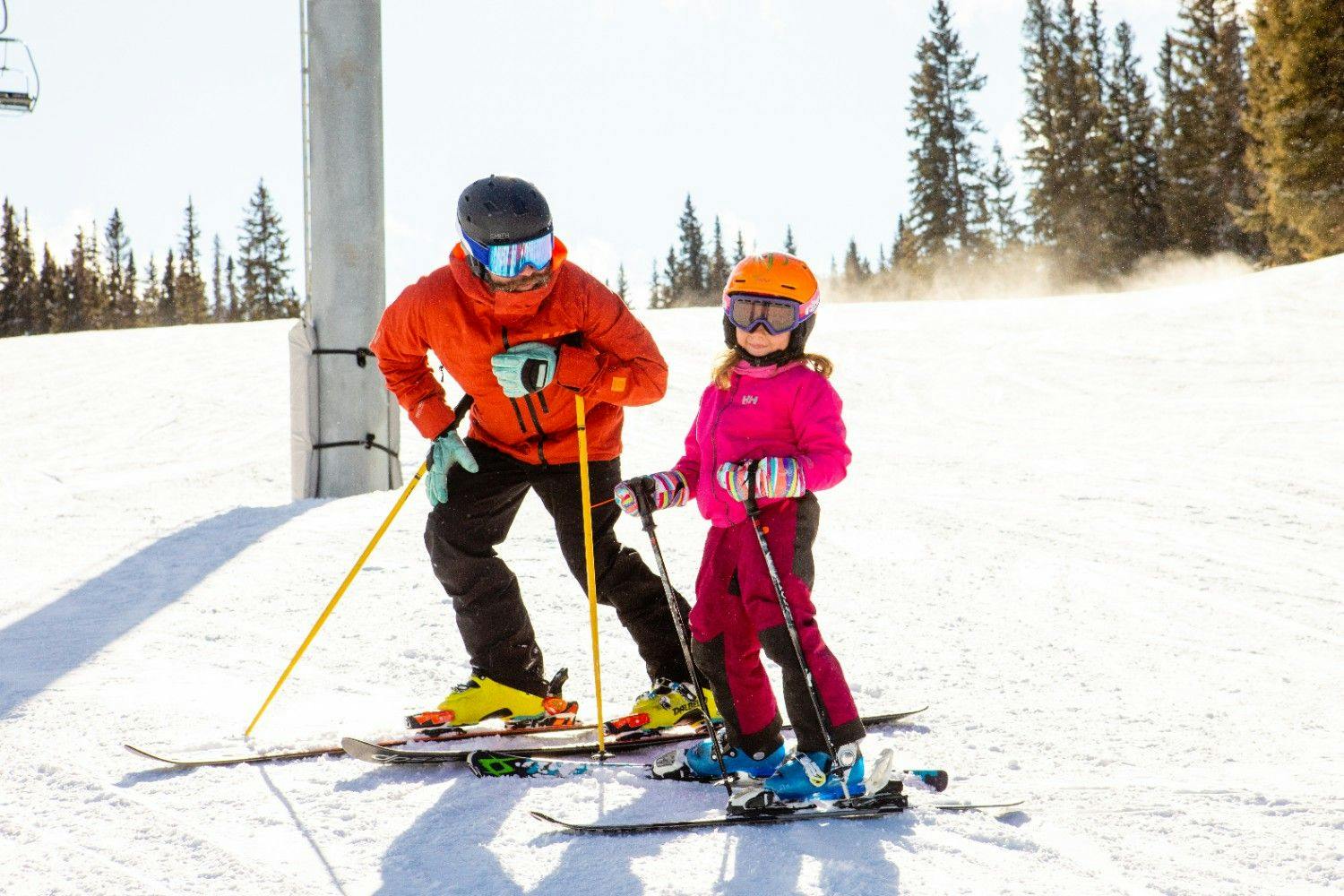 Ski instructor standing next to young girl on skis on the slopes at Aspen Snowmass Ski Resort