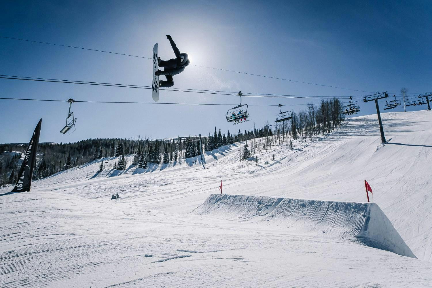 Snowboarder does a grab in the air on a sunny day at Aspen Snowmass terrain park