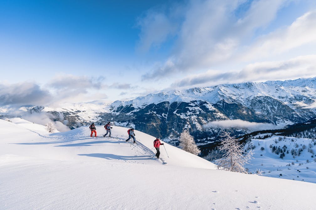 A group of 4 skiers treks along the top of a snowy mountain on a bluebird day in Verbier 4 Vallées in Switzerland